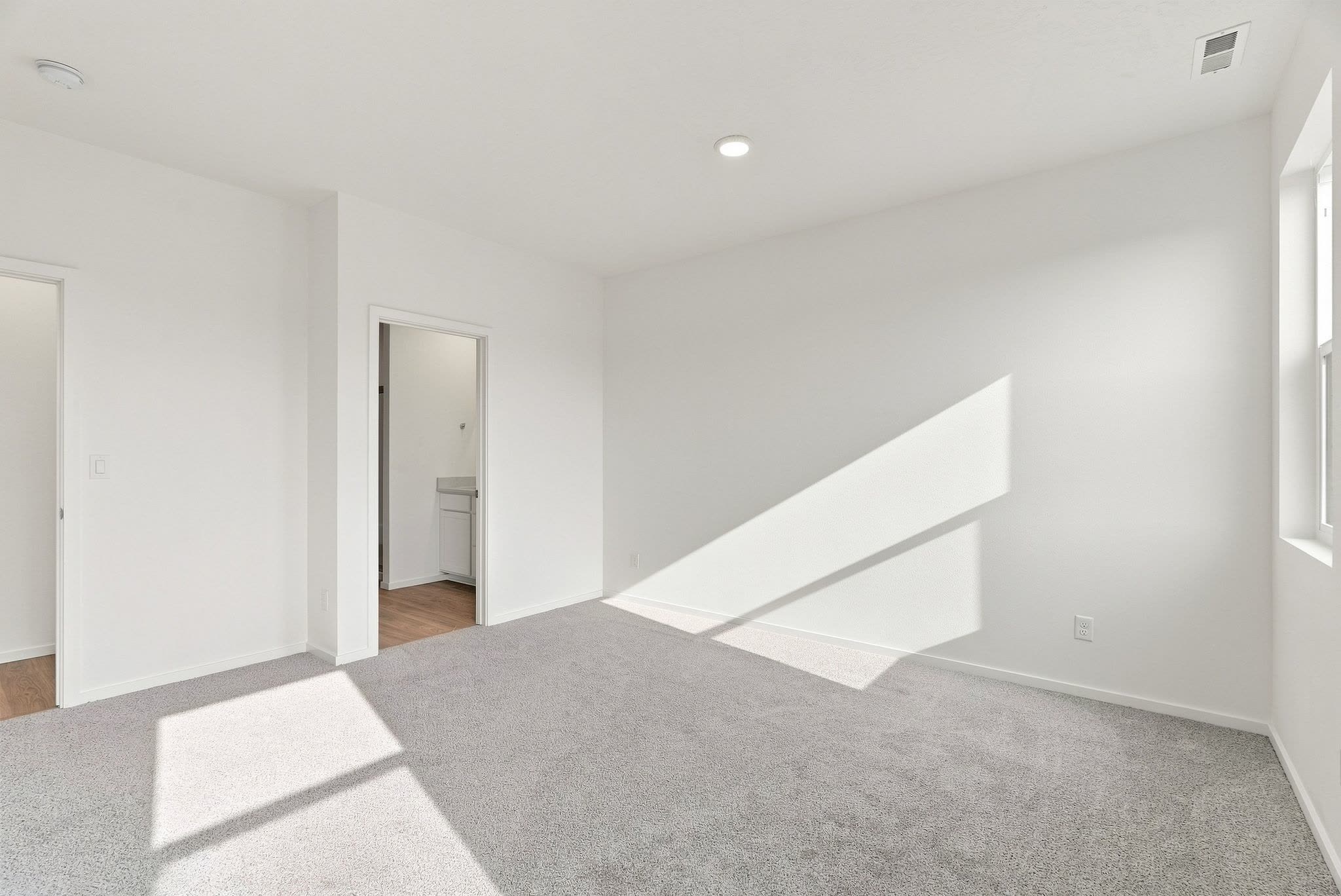 The carpeted primary bedroom, with the ensuite bath through the doorway.