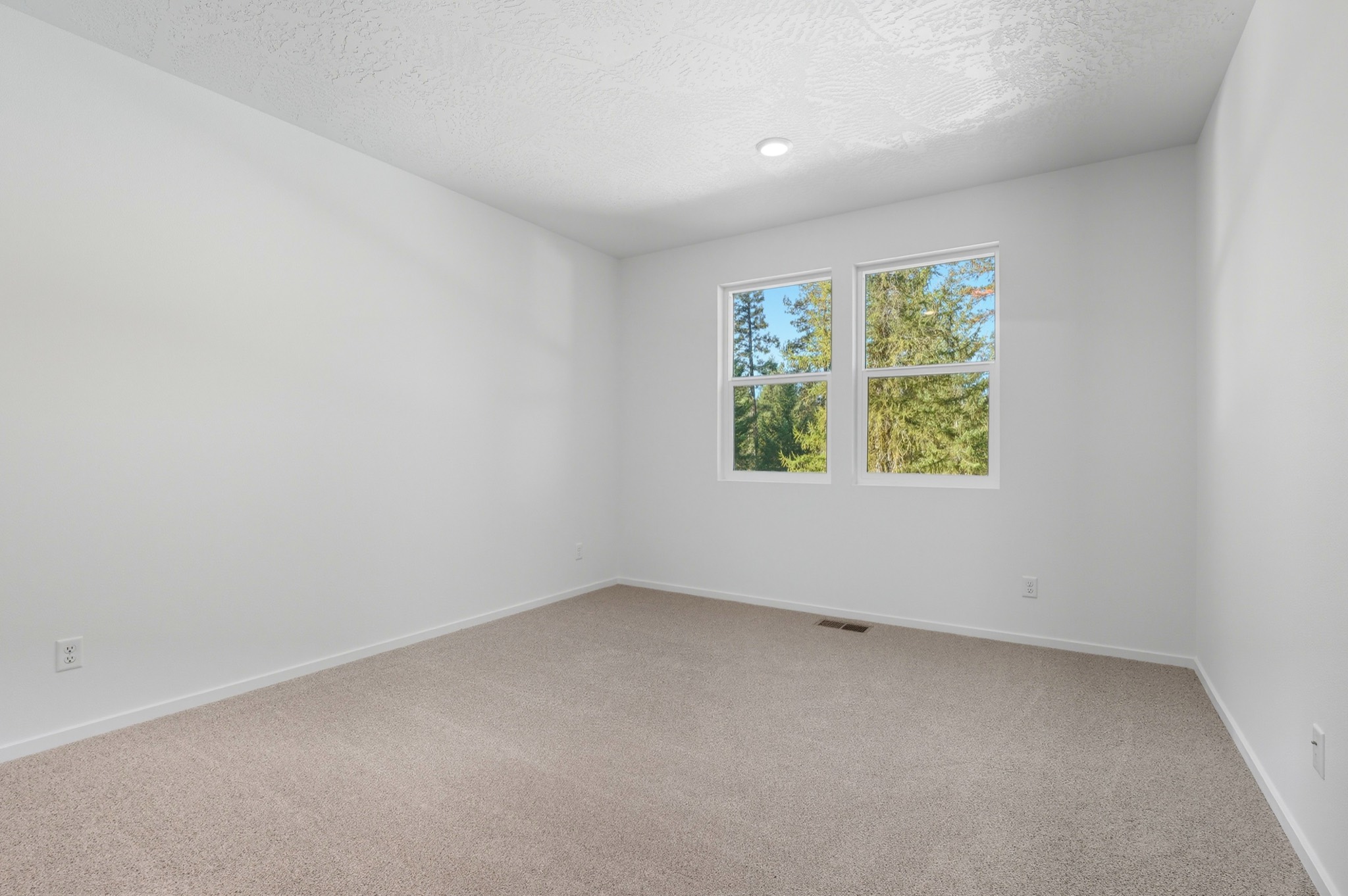 The Clark Fork plan: a carpeted secondary bedroom with two windows looking into the pines.