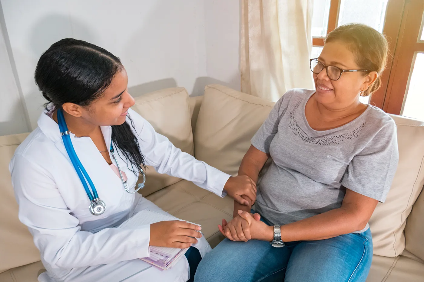 Doctor speaks with an older woman during a home visit while holding her hand.