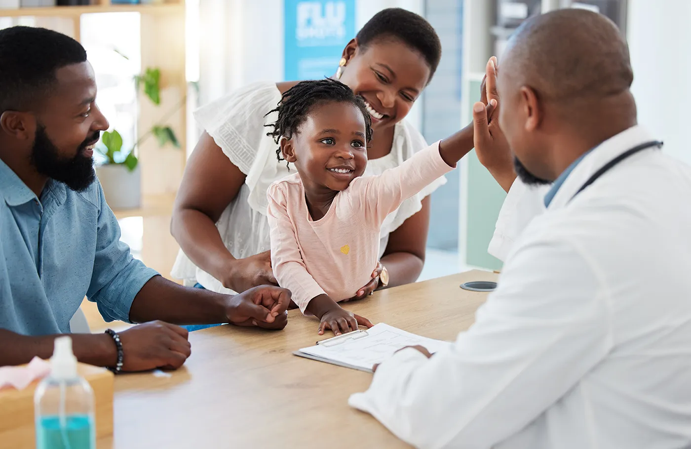 Parents and their young daughter meet with a doctor at a table in a medical office.