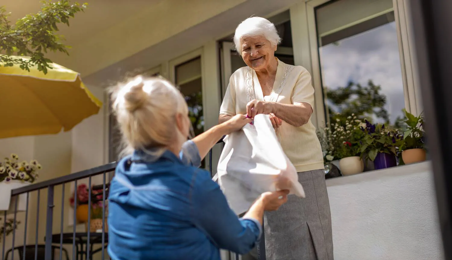 Volunteer hands a grocery bag to an older woman standing outside her home.