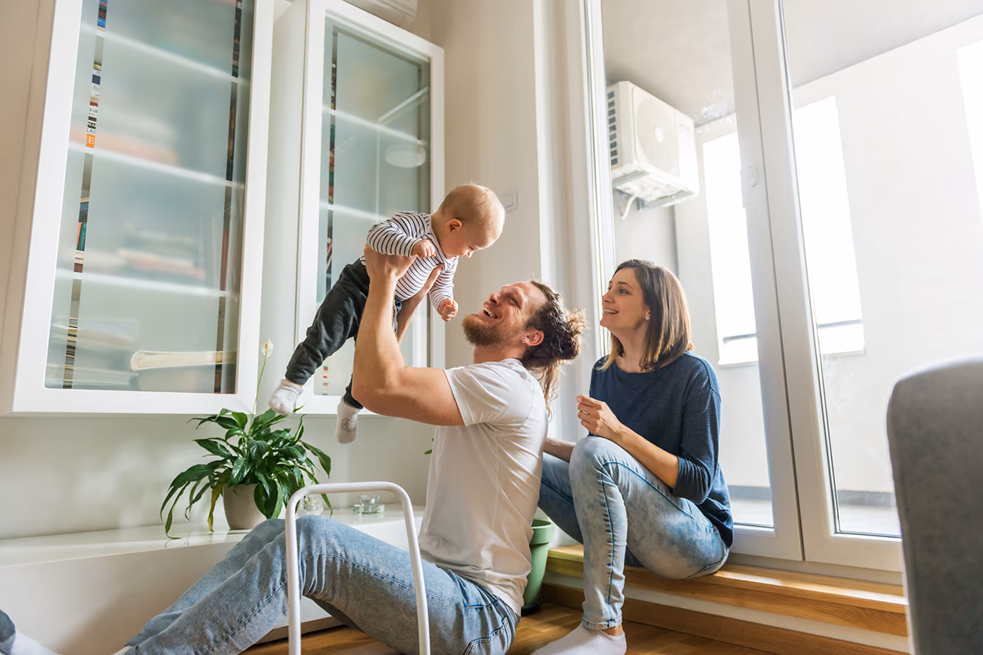 Parents play with their baby in a bright living room.