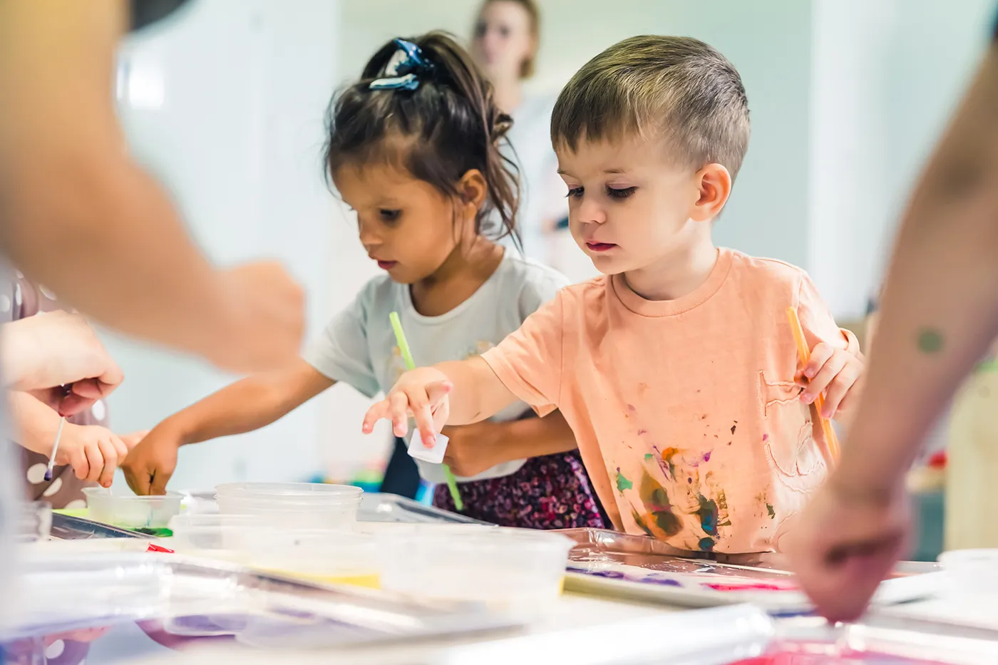 Two young children paint and make art together at a classroom table.