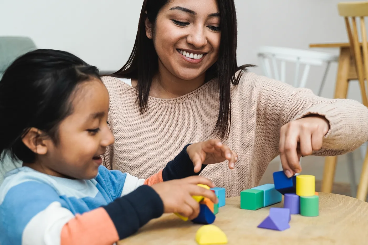 Woman helps a young child play with colorful learning blocks at a table.