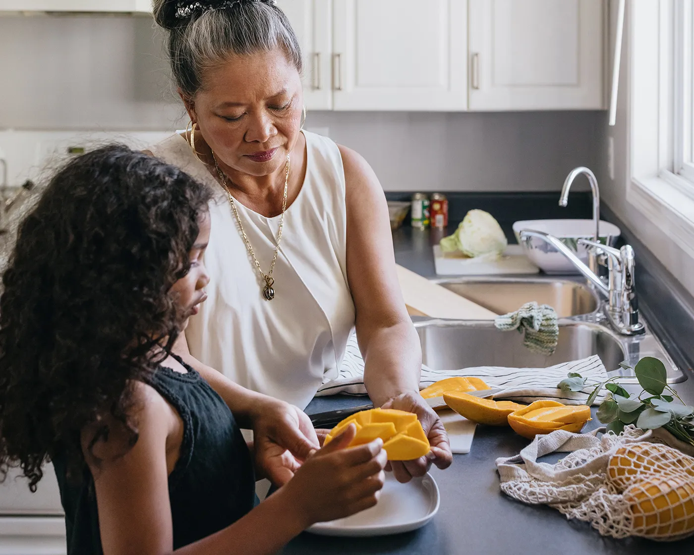 Woman and child preparing fresh fruit together at a kitchen sink.
