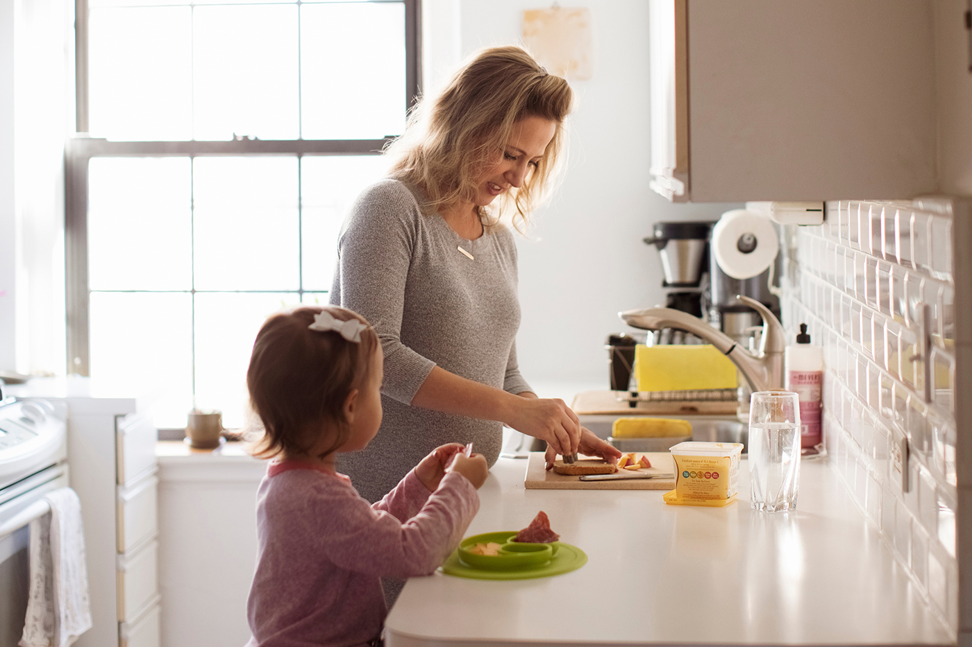 Parent and young child prepare food together at a kitchen counter.