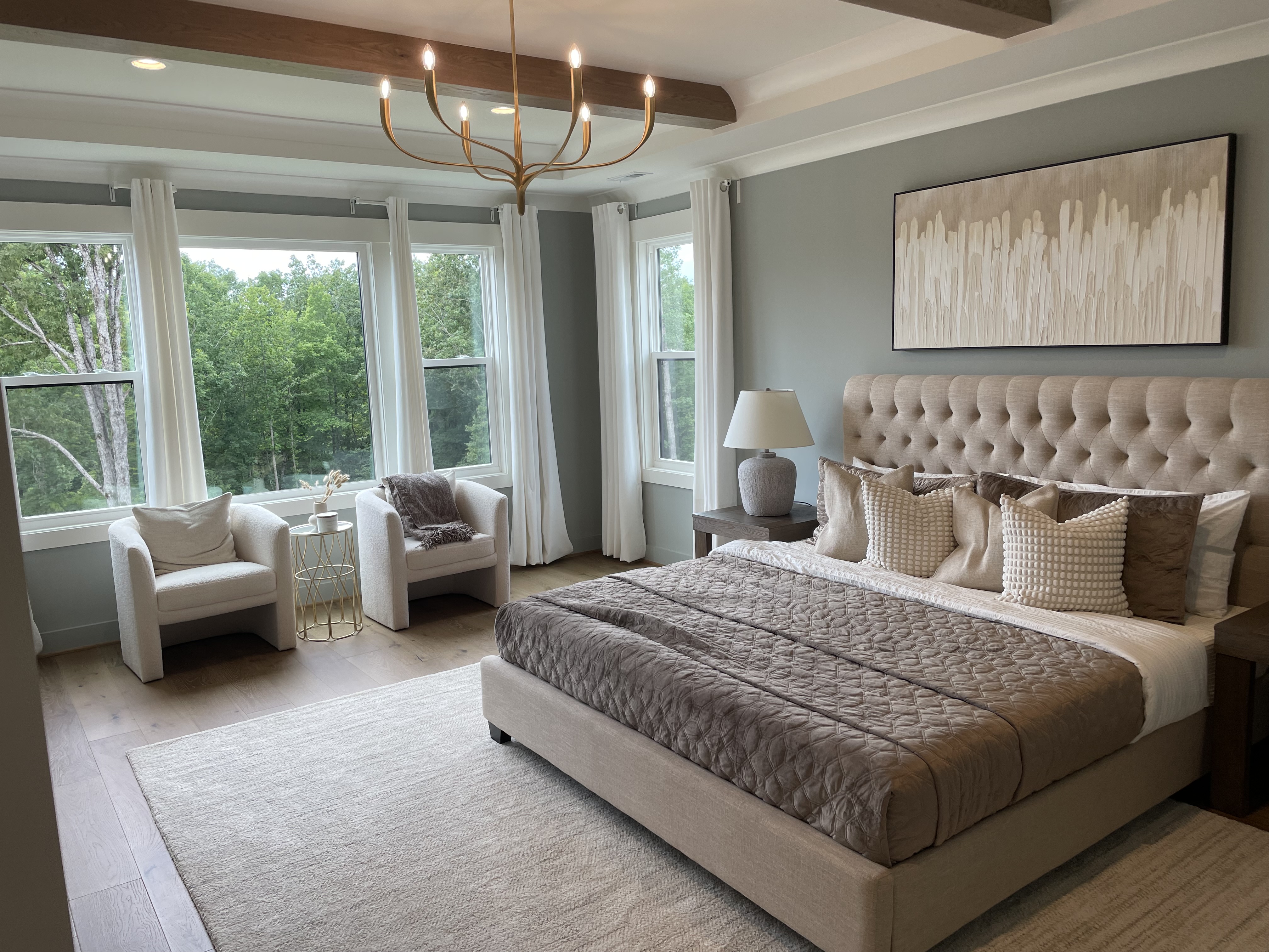 Serene primary bedroom with large windows overlooking a wooded setting