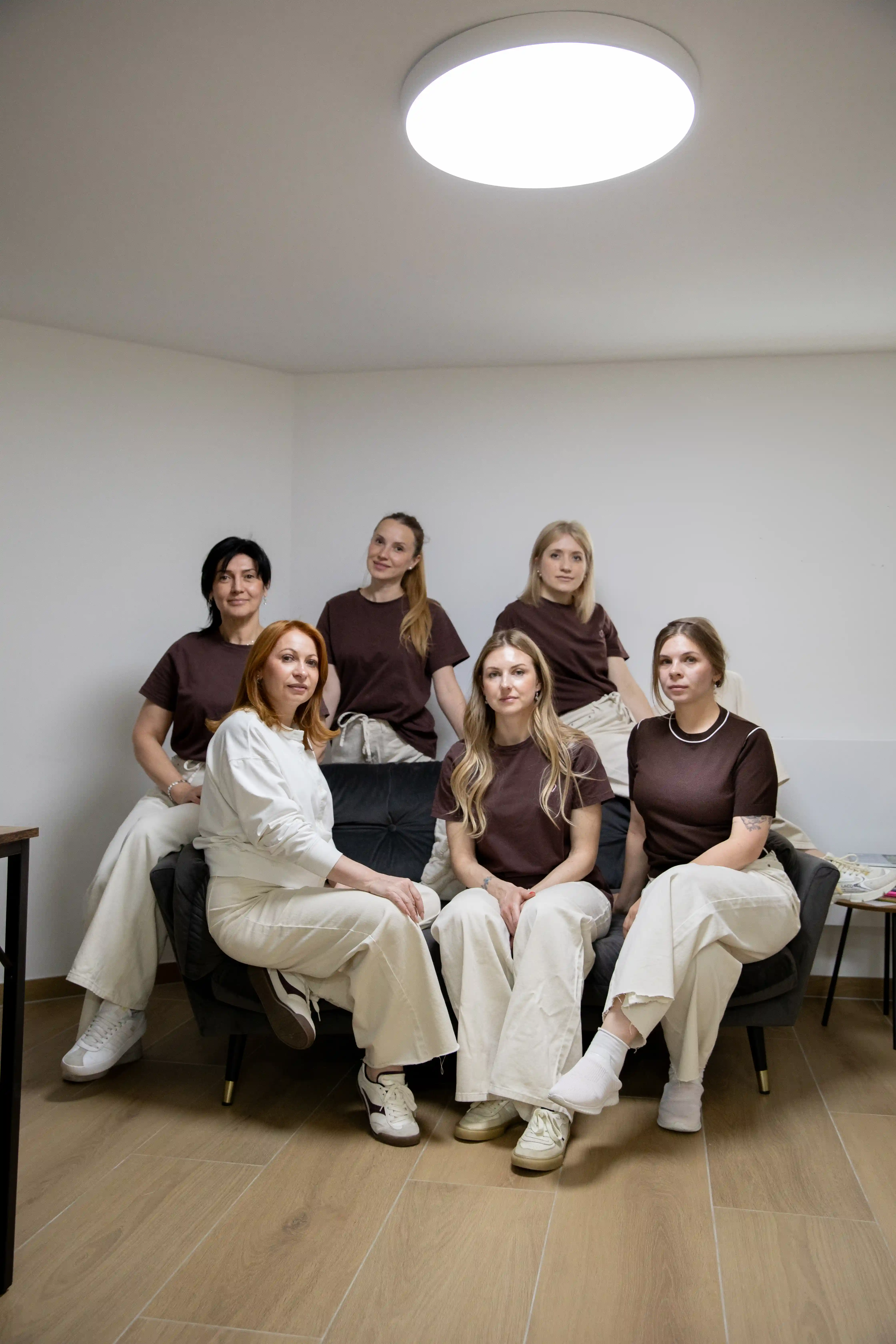 Sechs Mitarbeiterinnen des Felena Studios in braunen Shirts auf dem Sofa im Studio