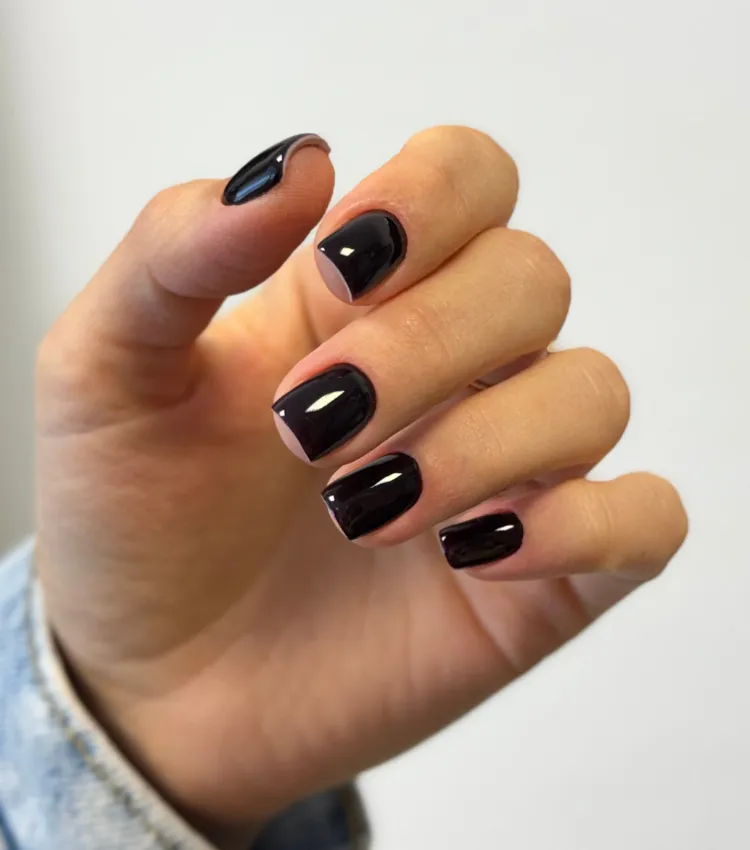 Kurze eckige Gelnägel in glänzendem Schwarz auf gepflegter Hand