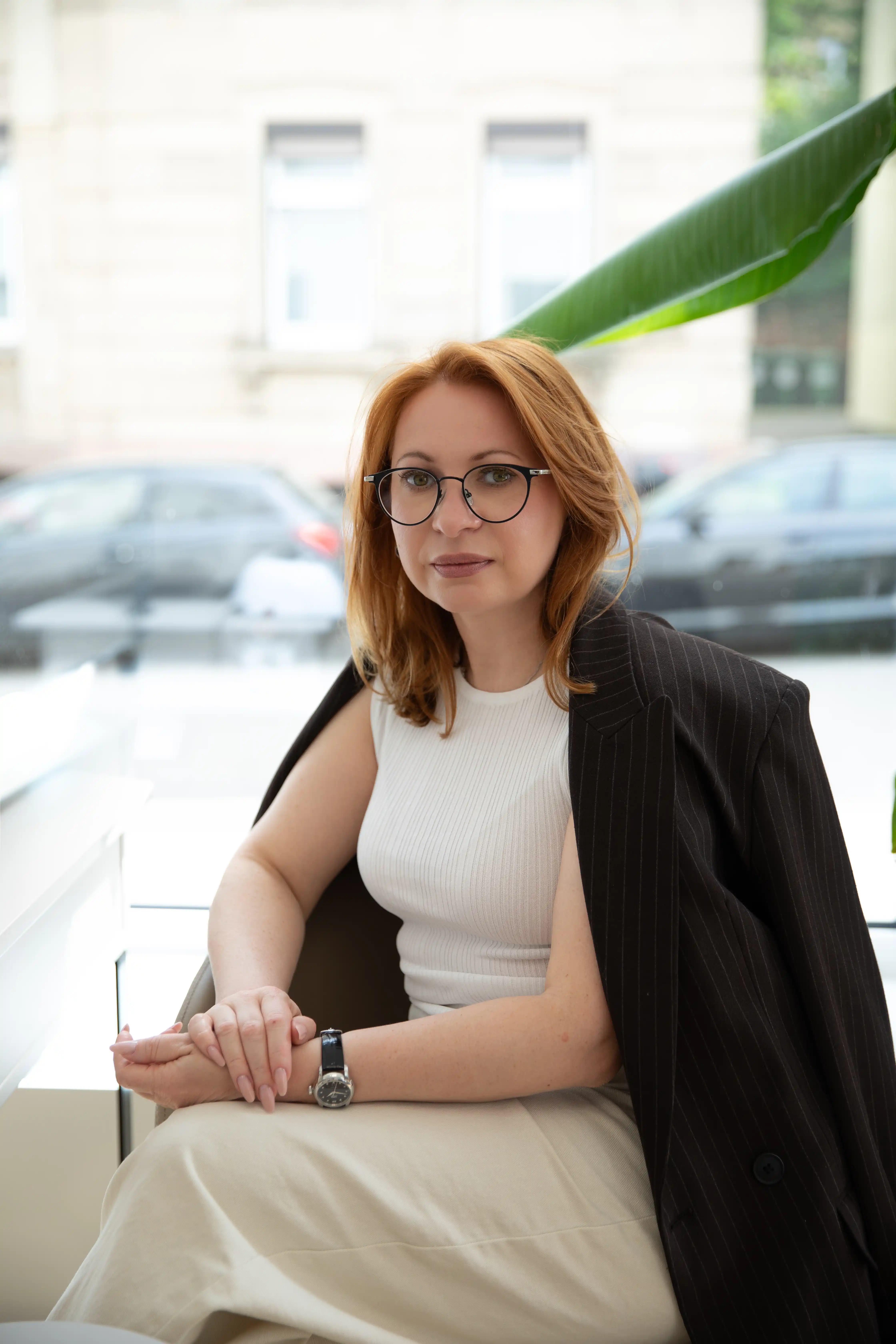 Rothaarige Mitarbeiterin mit Brille und Blazer sitzt am Fenster des Felena Studios