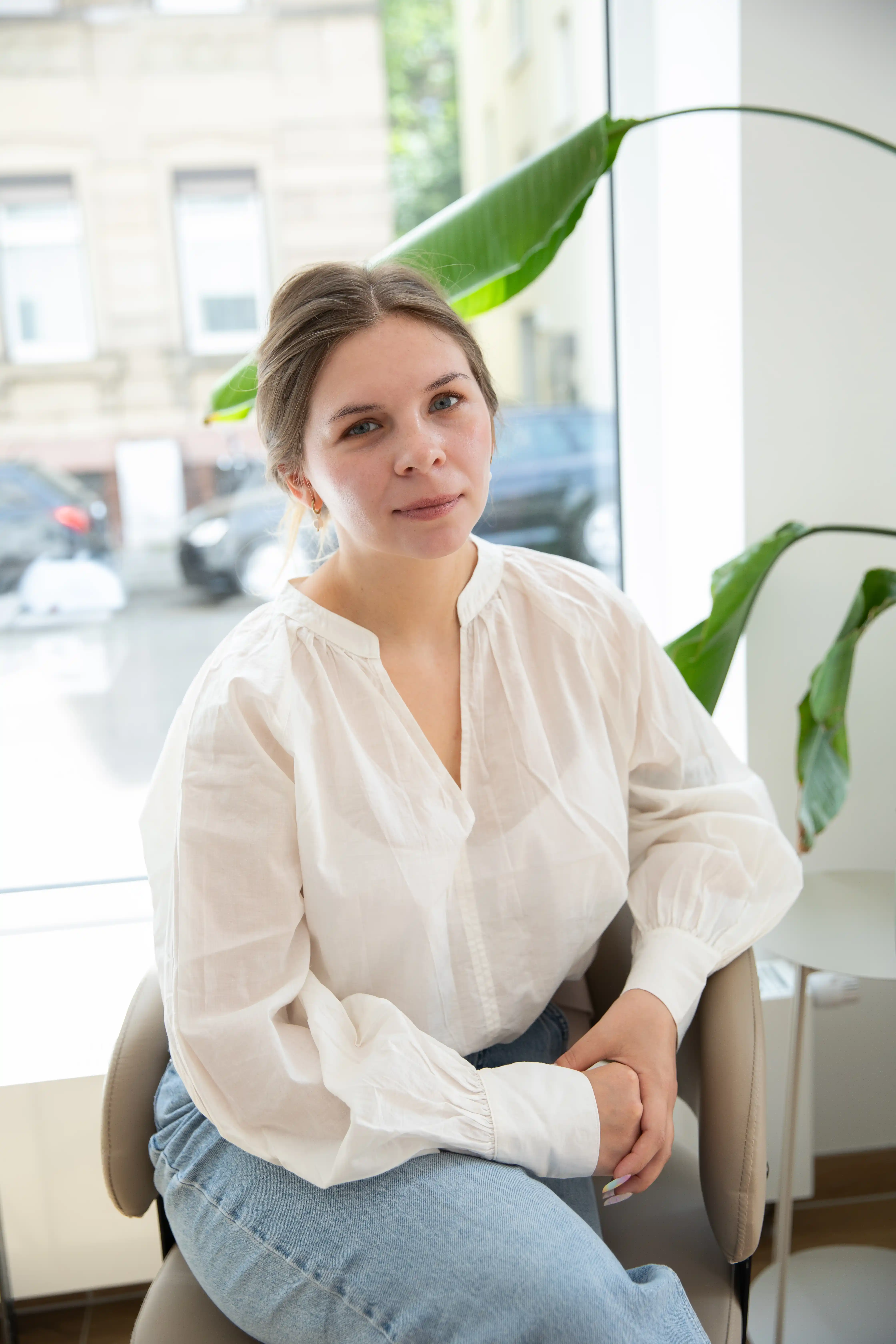 Mitarbeiterin des Felena Studios in weißer Bluse im Sessel neben einer Strelitzie