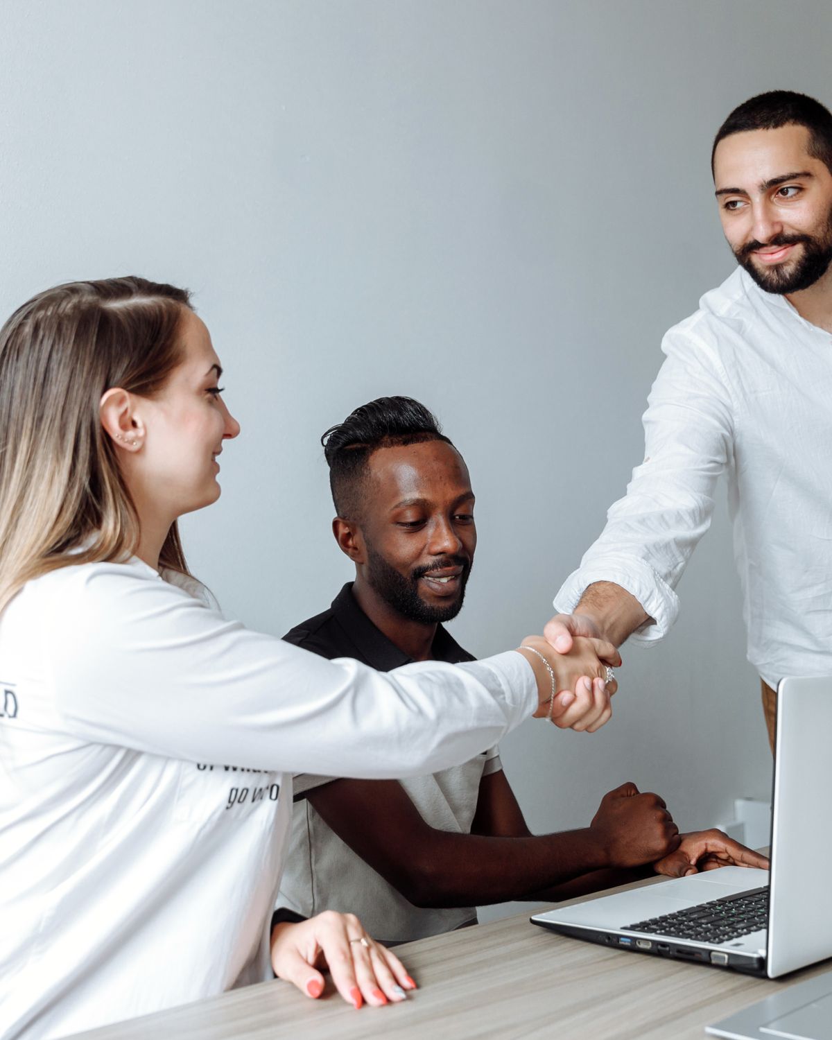 Smiling colleagues shaking hands across a desk after an interview
