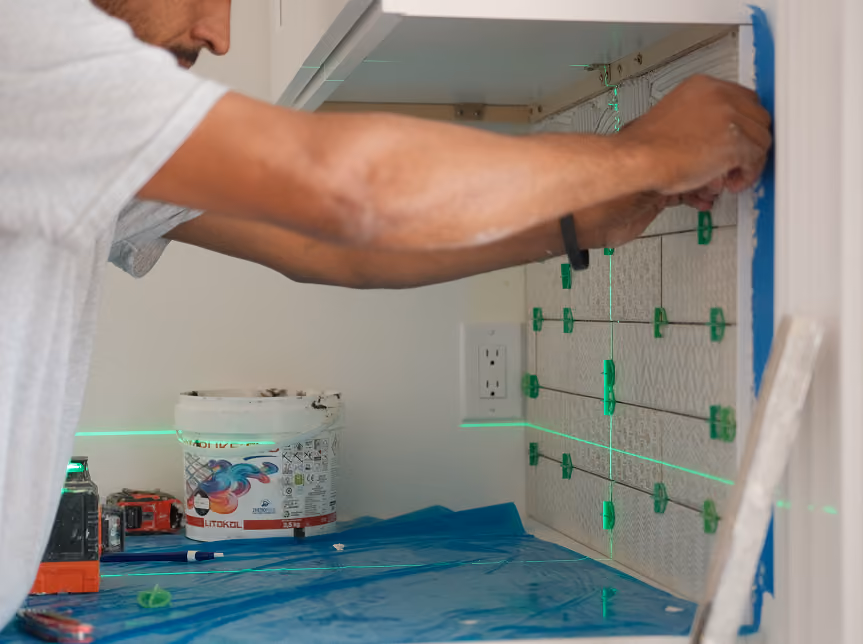 Tile installer using a laser level and spacers to set wall tile