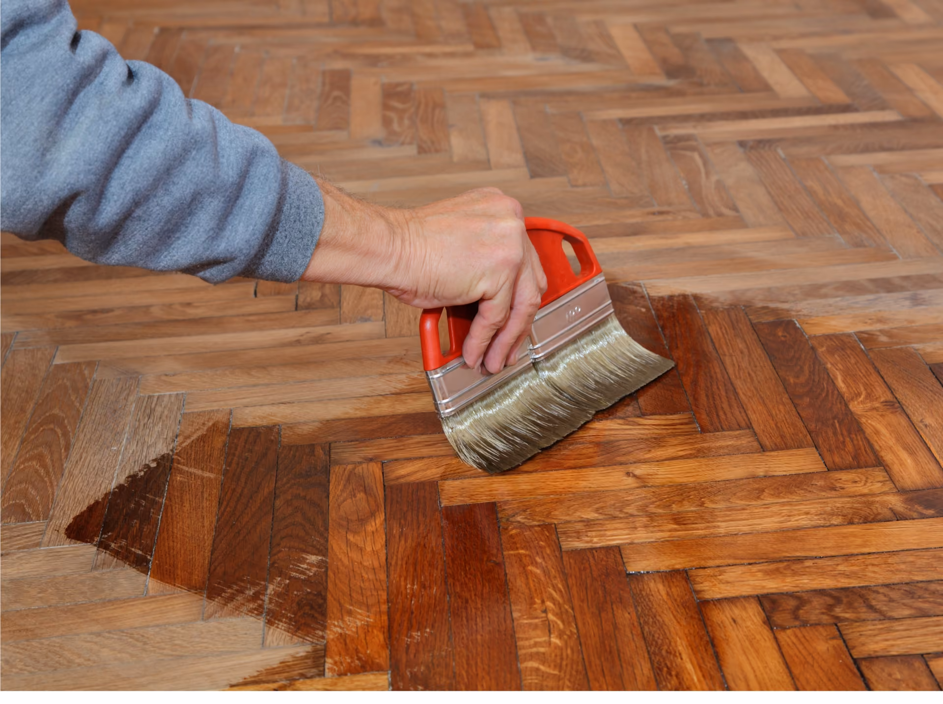 Technician applying stain to a herringbone hardwood floor with an applicator pad