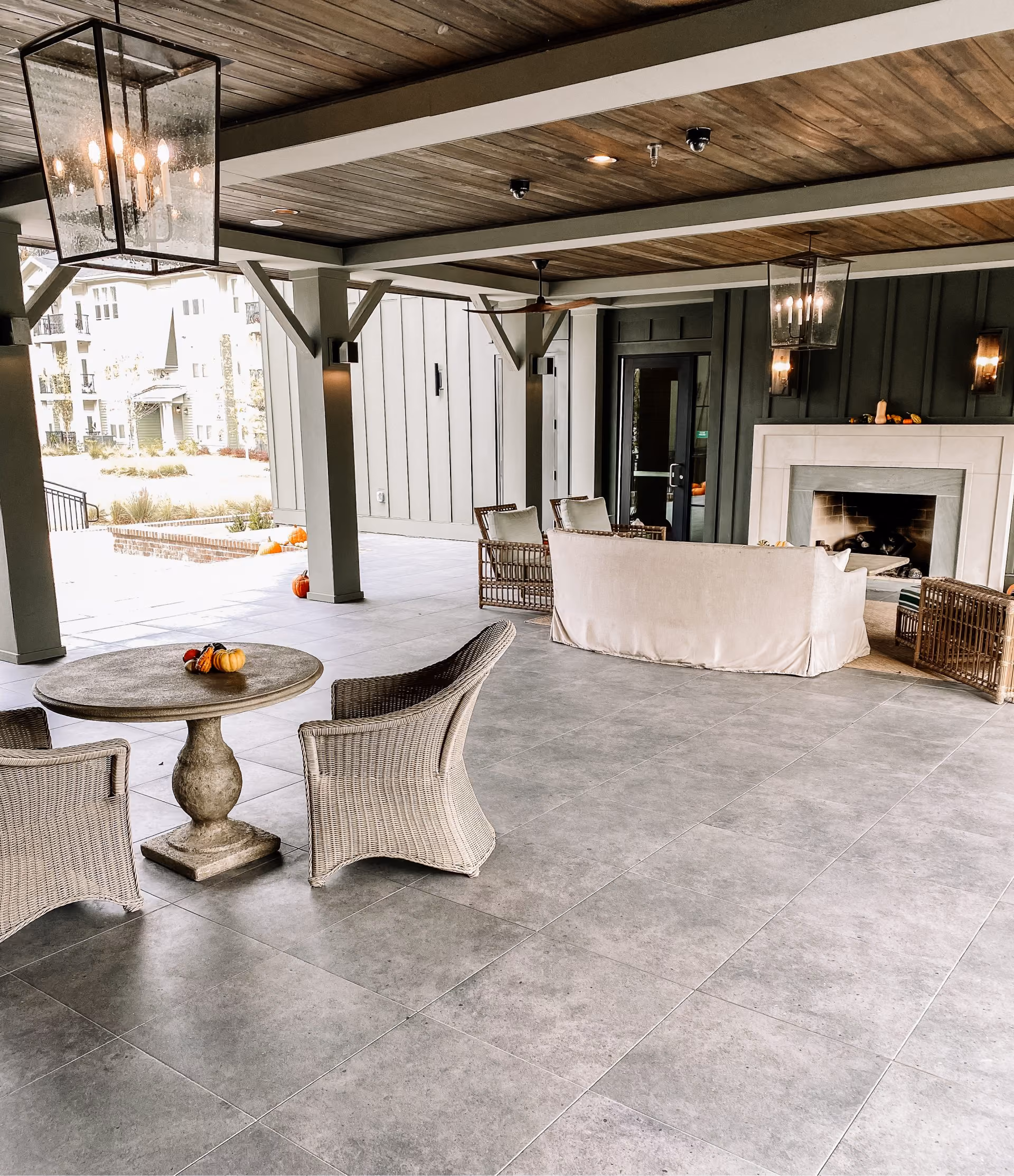 Covered patio with concrete-look tile flooring, an outdoor fireplace, and wicker furniture