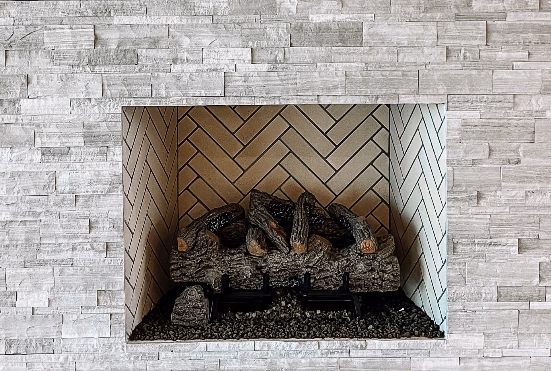 Fireplace with a stacked natural stone surround and herringbone tile firebox