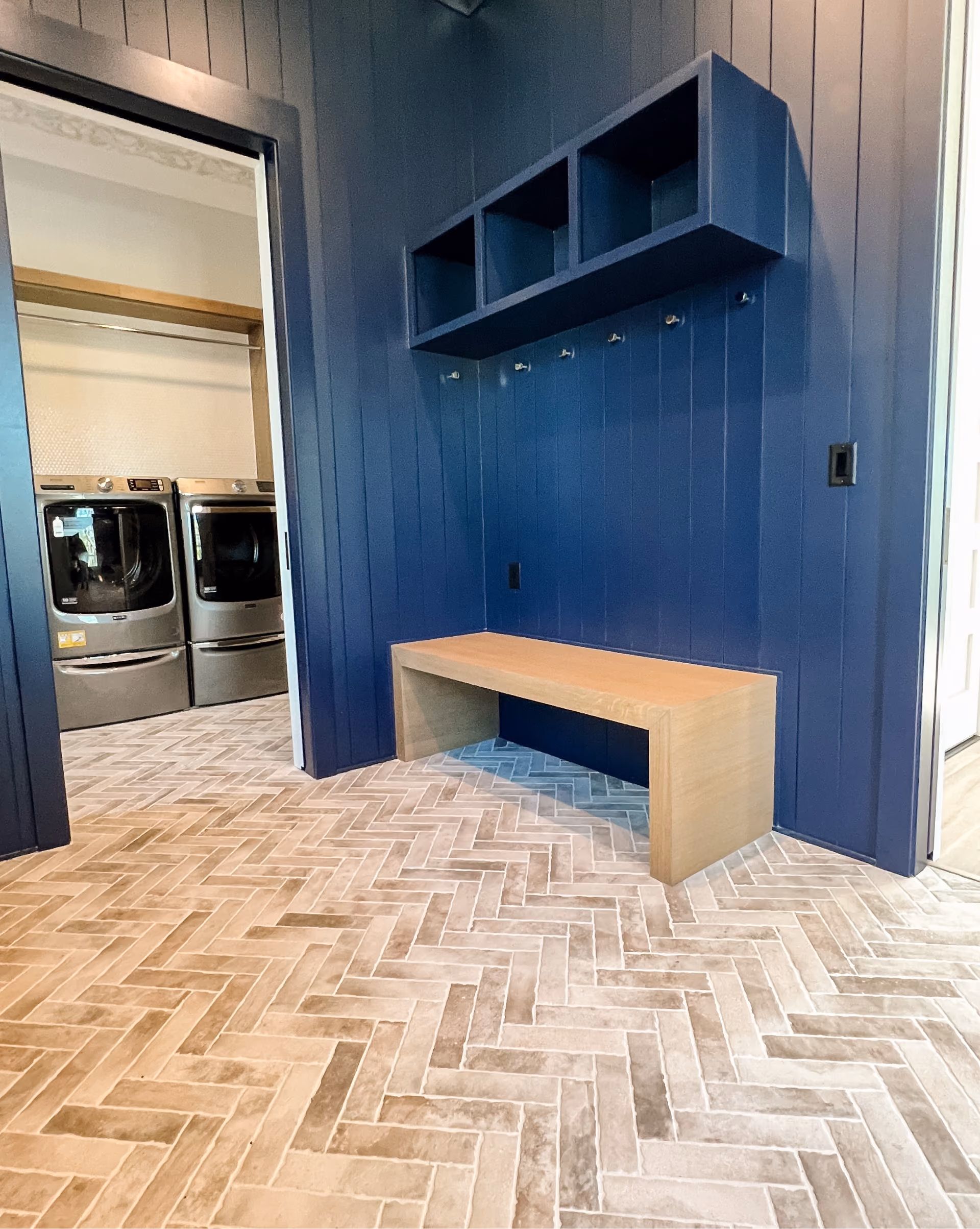 Laundry room with herringbone natural stone tile flooring and navy cabinetry