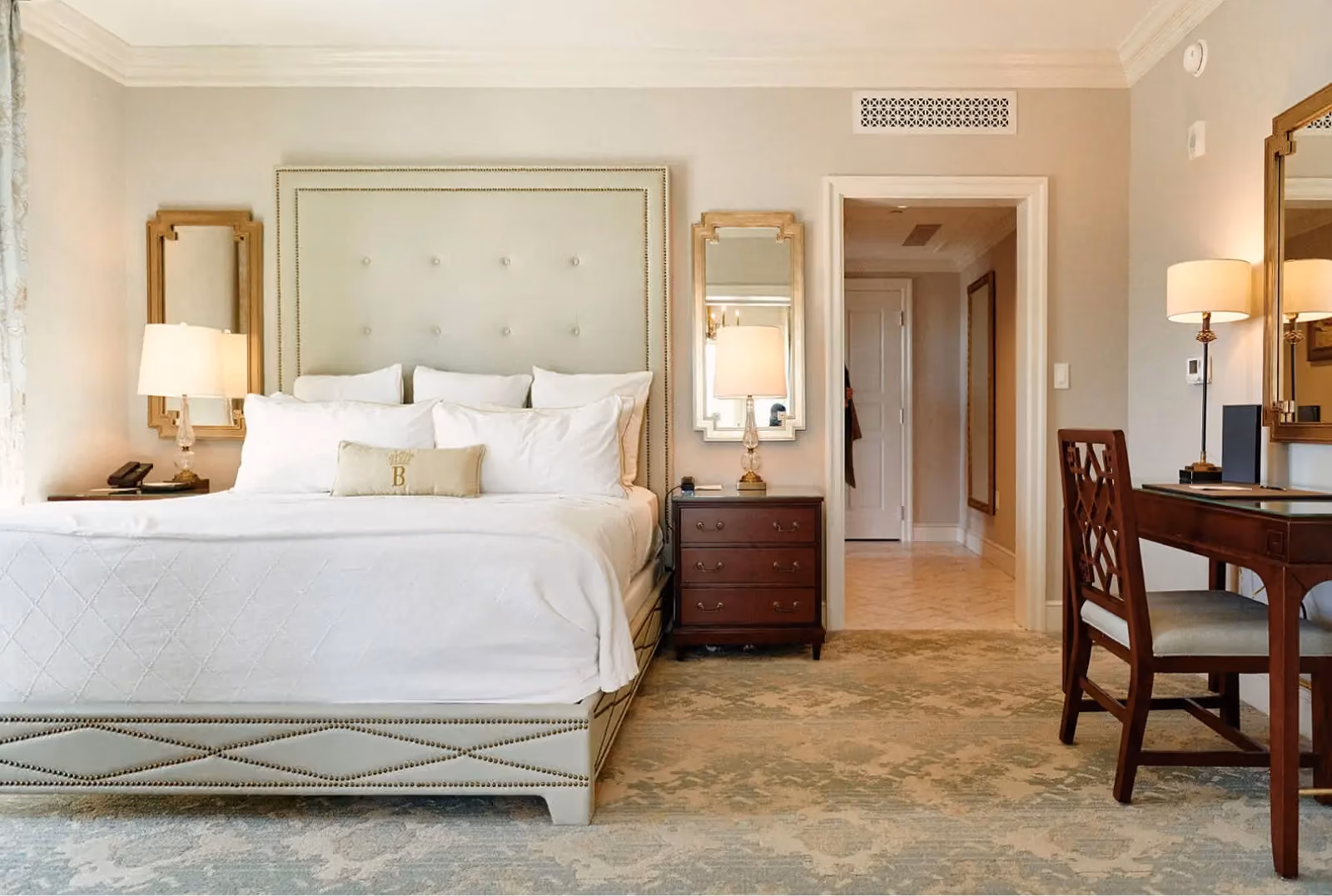 Hotel guest room with tan patterned carpet and an upholstered headboard