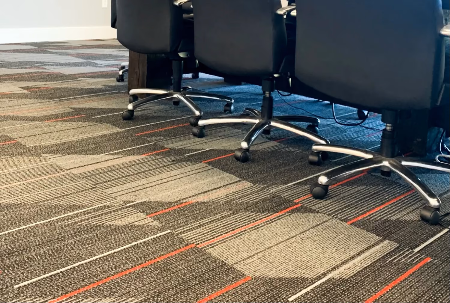 Close-up of office carpet tile with red accent stripes beneath rolling chairs