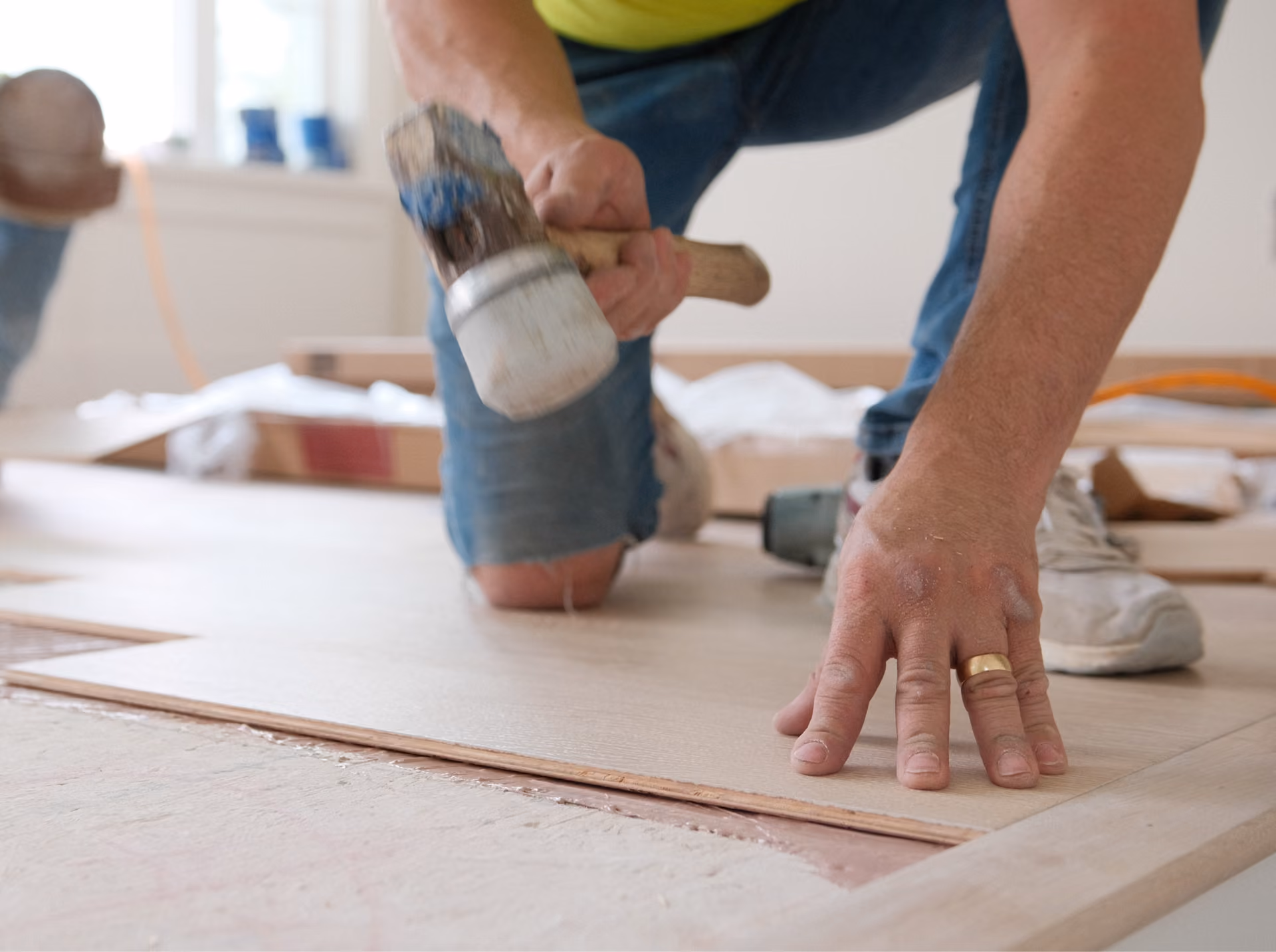 Installer using a tapping block to fit hardwood plank flooring