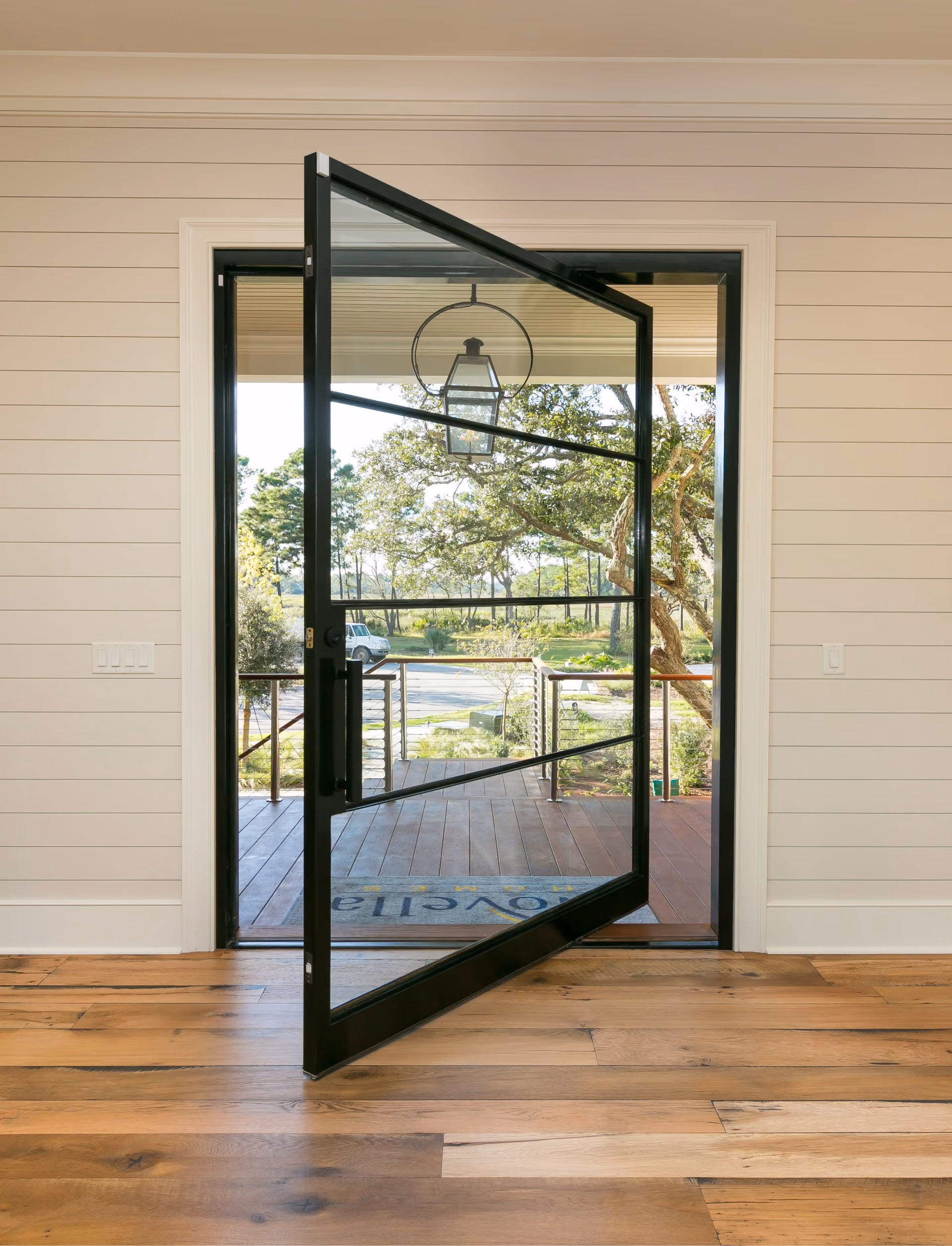 Glass pivot entry door opening to a porch, with hardwood flooring