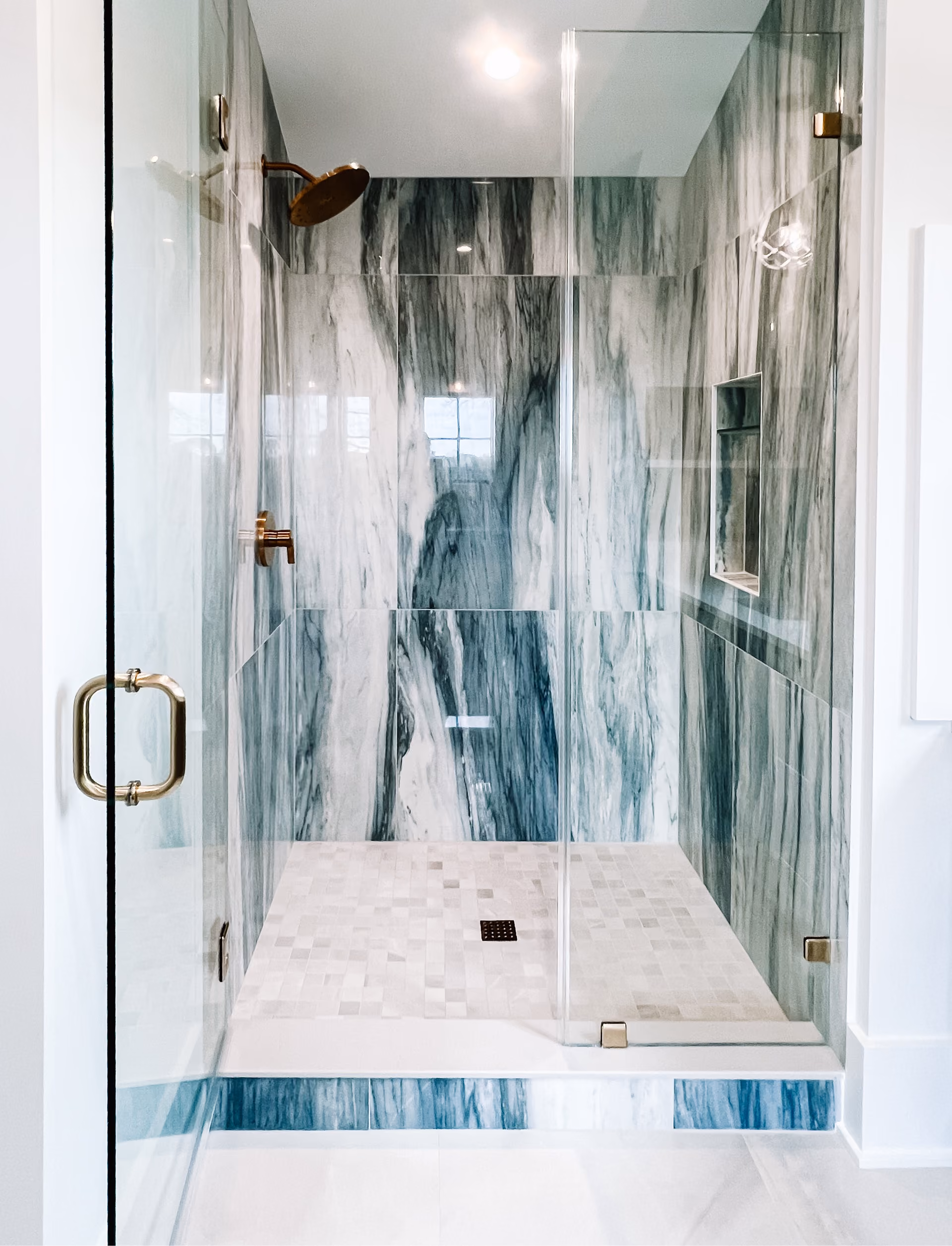 Glass shower with green-gray marble tile walls and a marble mosaic floor