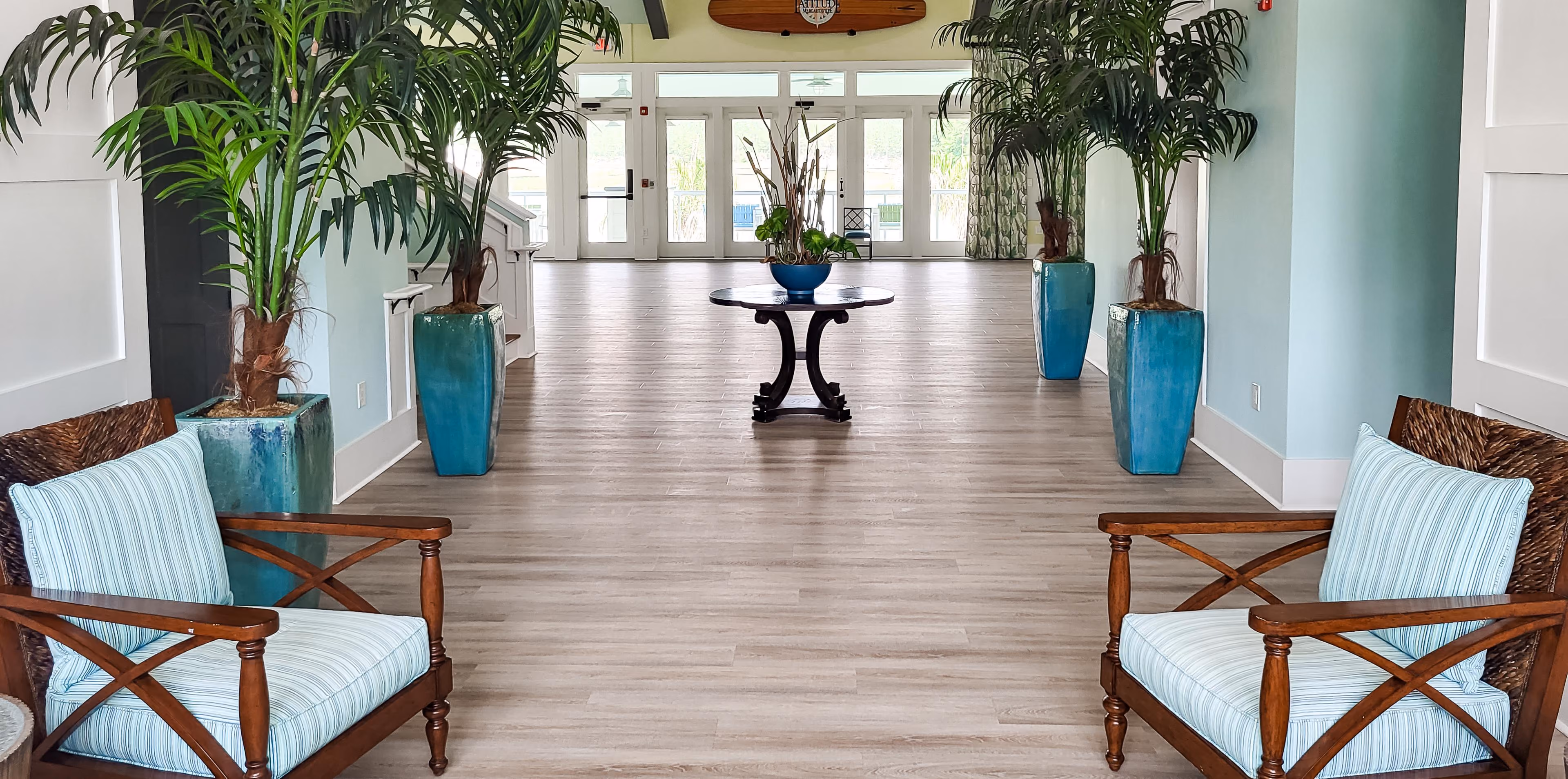 Hotel lobby with wood-look flooring and potted plants at a wide entryway