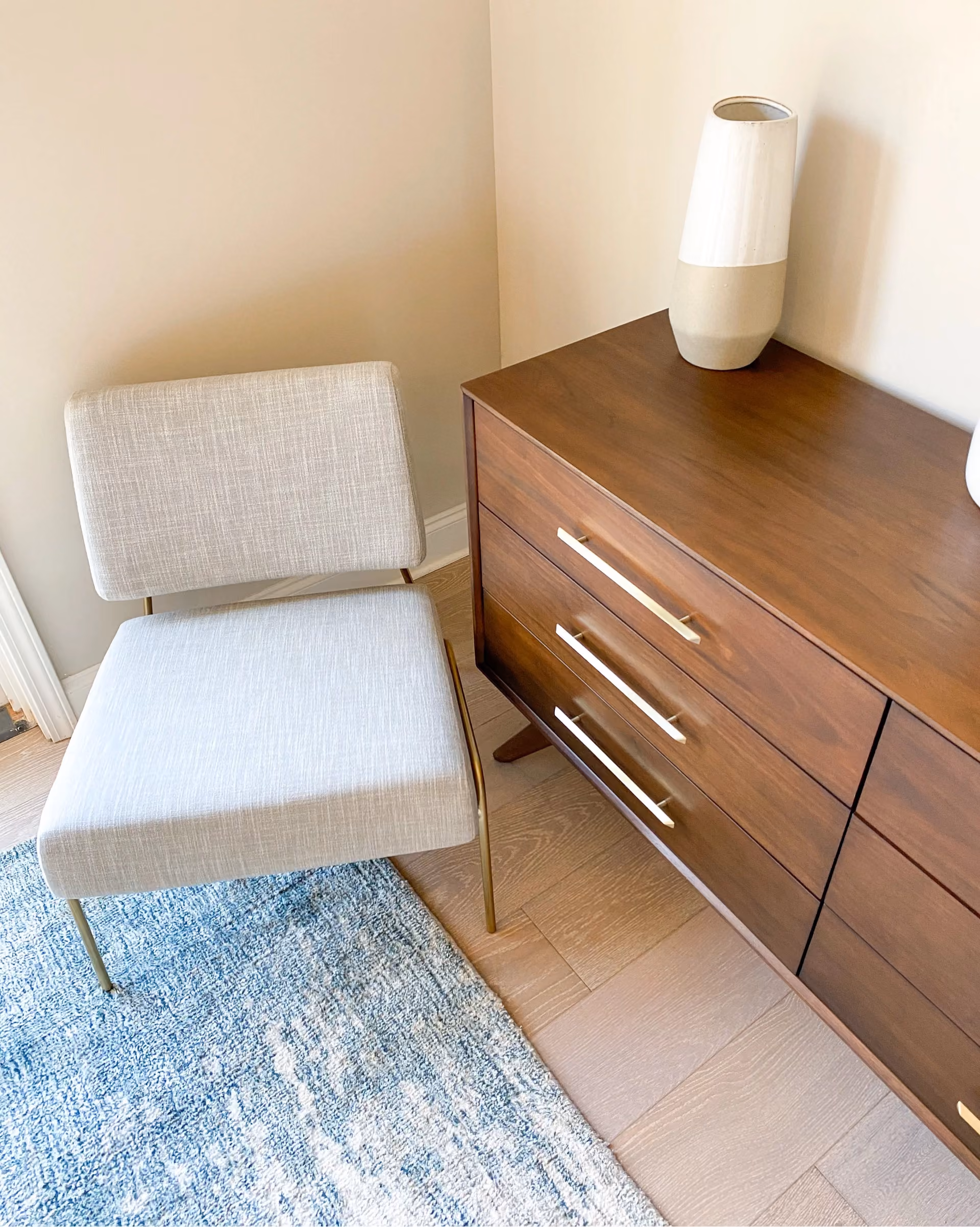 Student apartment bedroom with a tufted headboard, wood dresser, and patterned carpet flooring