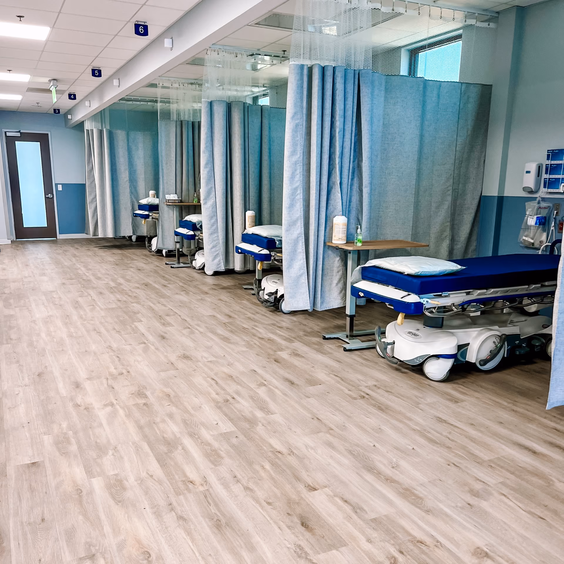 Healthcare facility hallway with hospital beds and light wood-look flooring