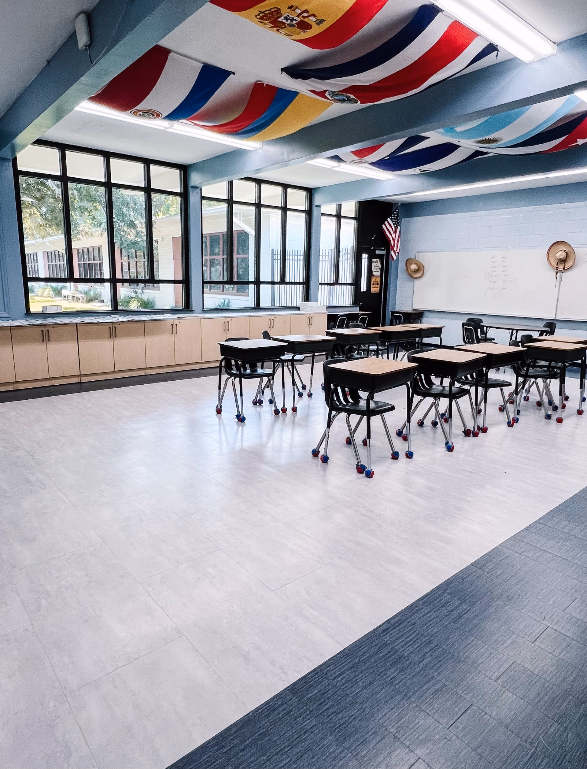 Classroom with desks, a glass wall partition, and dark wood-look flooring
