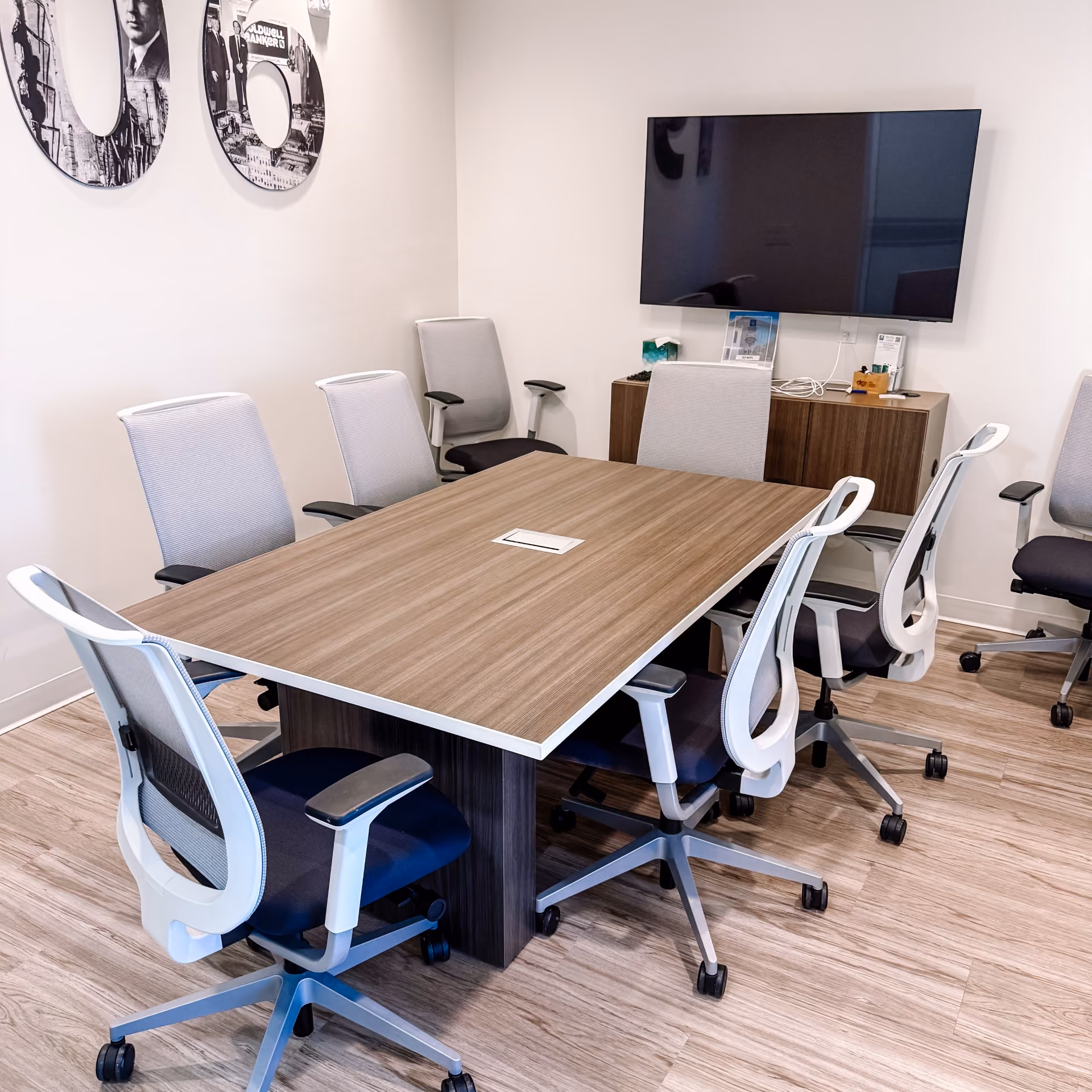 Office conference room with a wood table, gray mesh-back chairs, and light wood-look flooring