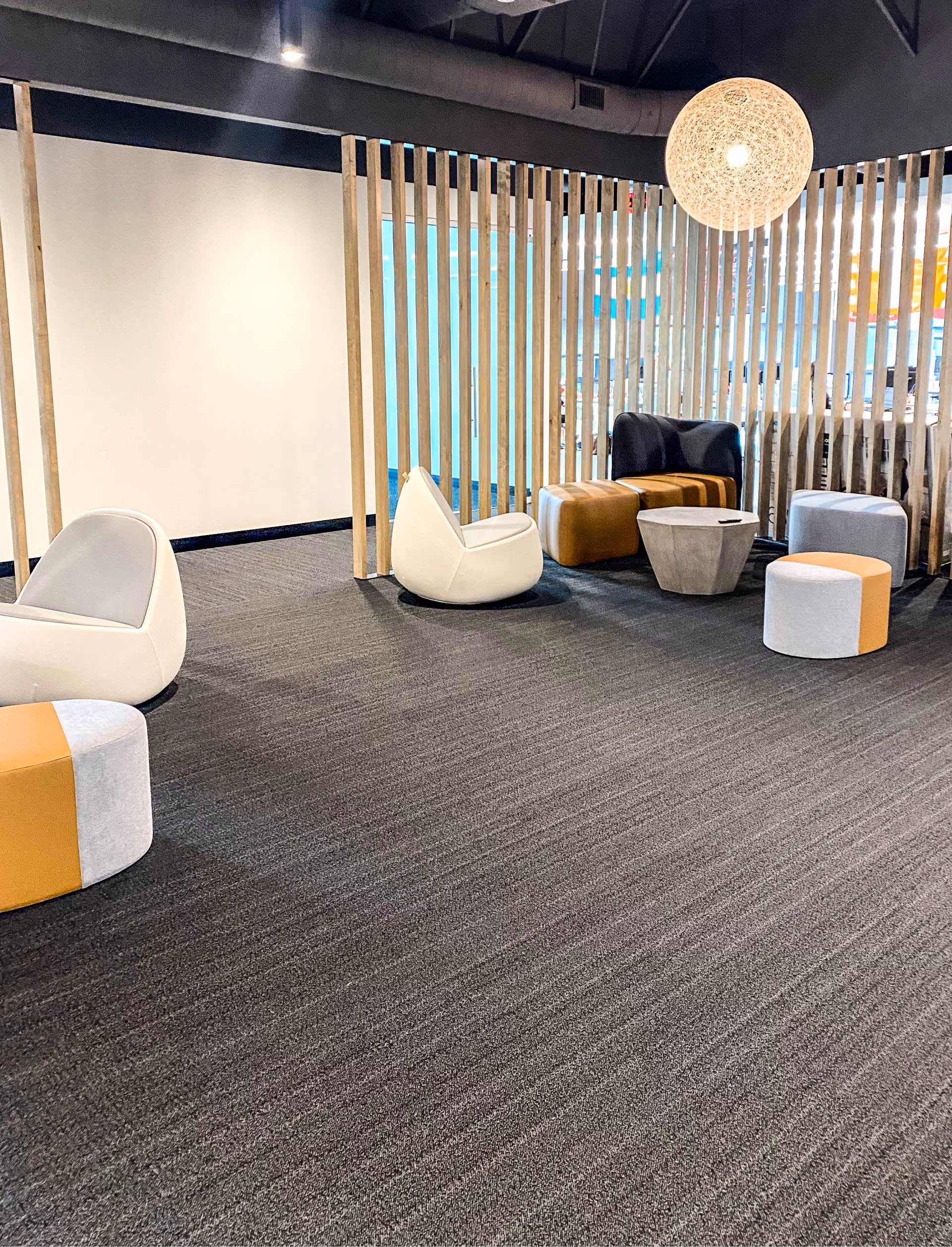 Office lounge nook with a colorful vertical-slat partition wall and dark carpet flooring