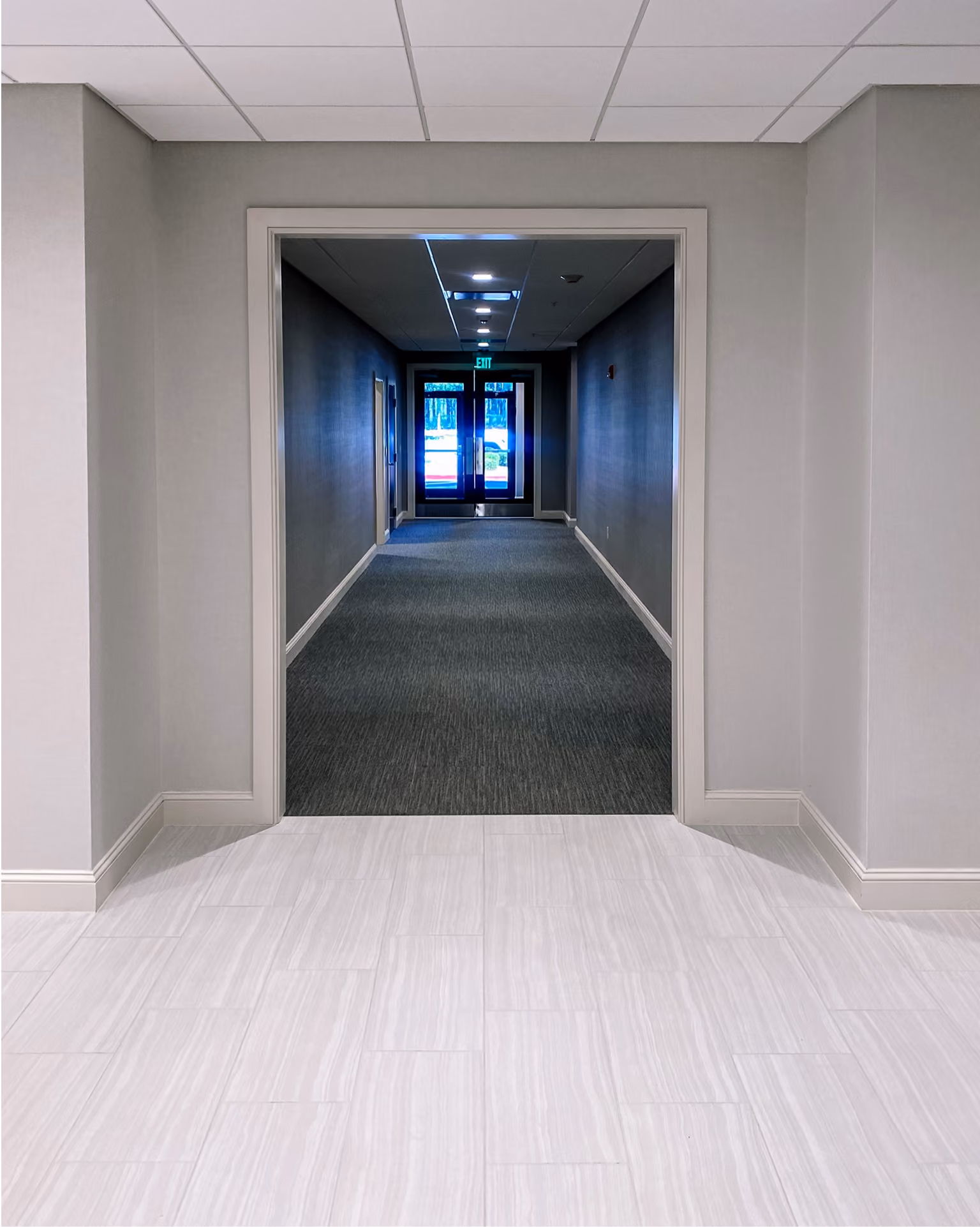 Bank hallway with dark carpet flooring leading to a light tile entryway