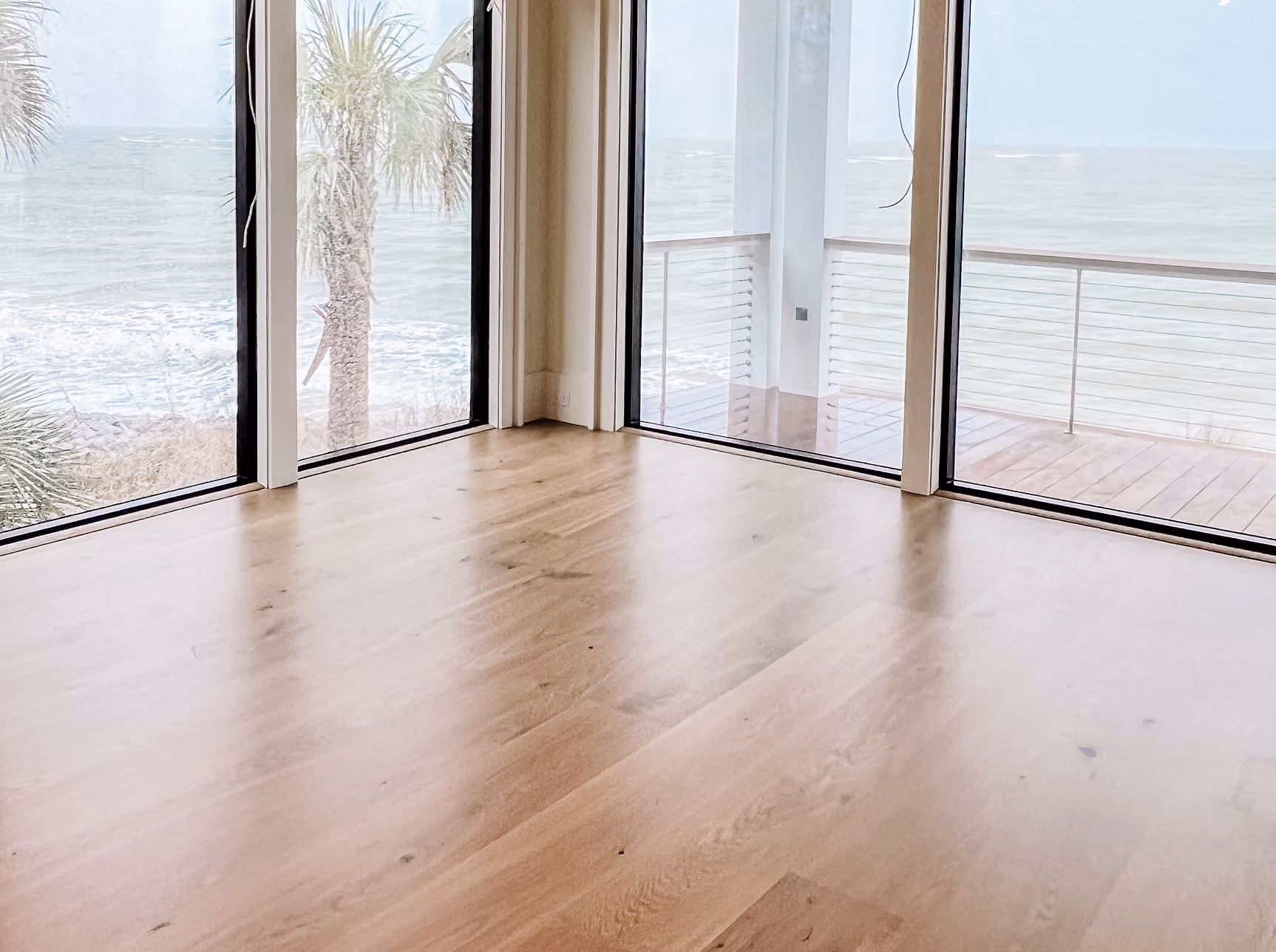 Residential living room with floor-to-ceiling windows overlooking the ocean and light hardwood flooring