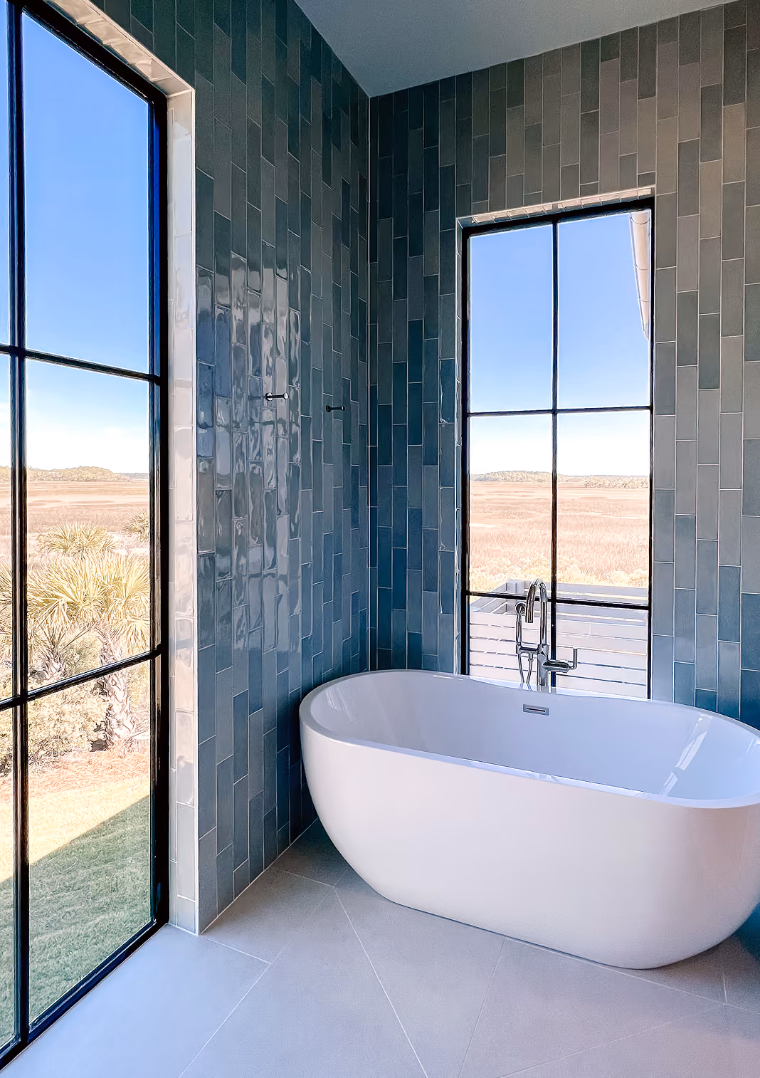 Residential bathroom with a freestanding tub, floor-to-ceiling windows, and a tile accent wall