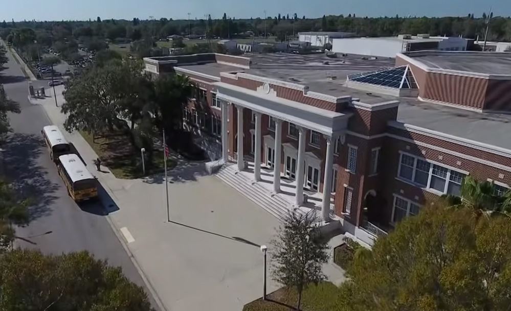 Aerial view of a brick school building with white columns and school buses parked out front