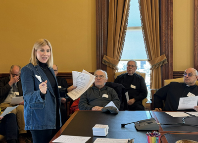 A blonde woman is speaking to a room of advocates about how to use their voices to make a difference. She is holding a pen in one hand and some papers in the other.