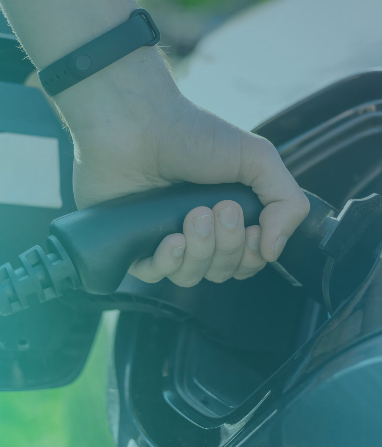 Hand holding a charging plug near an electric vehicle charging port.