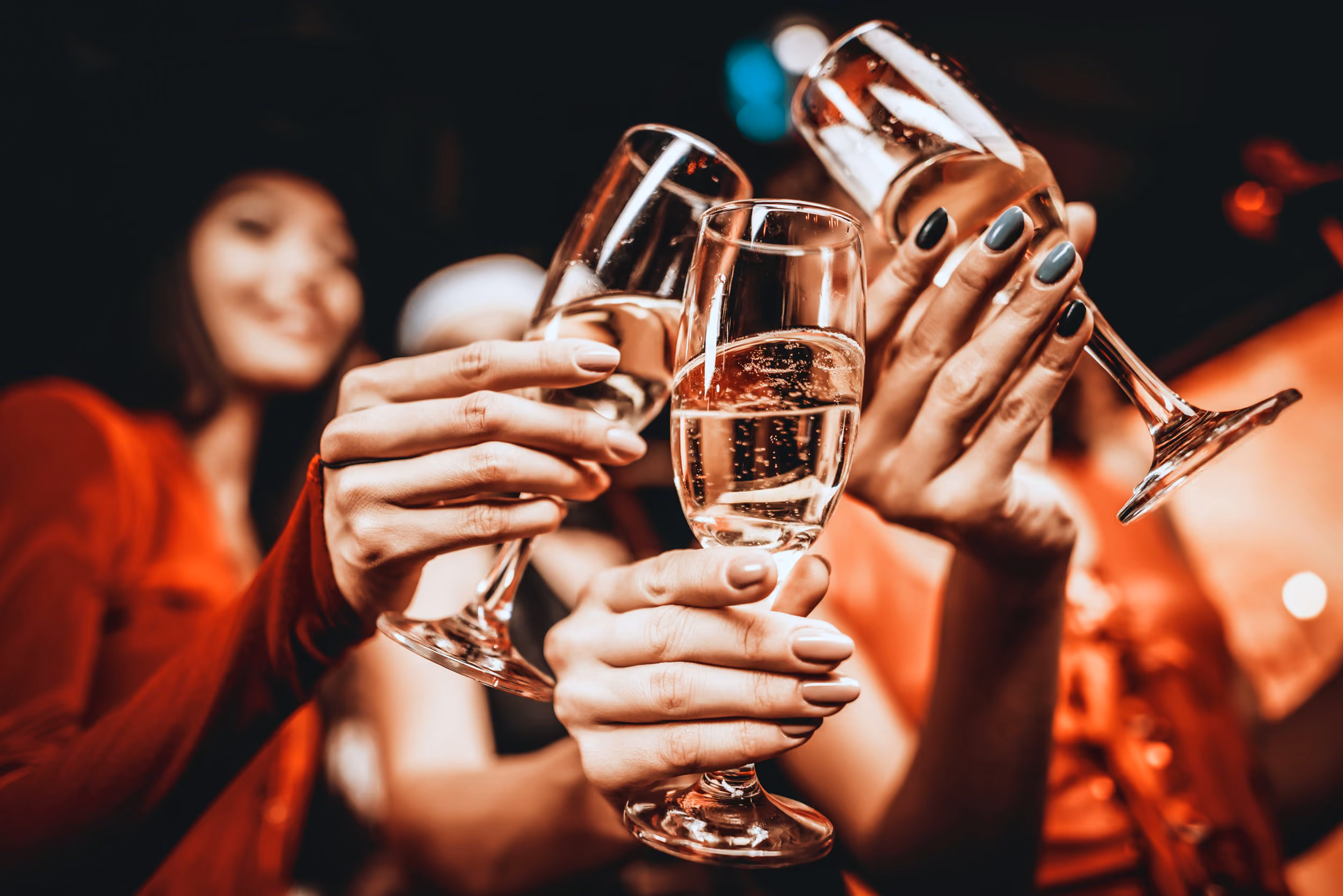 Three people clinking champagne glasses in a celebratory toast with blurred background.