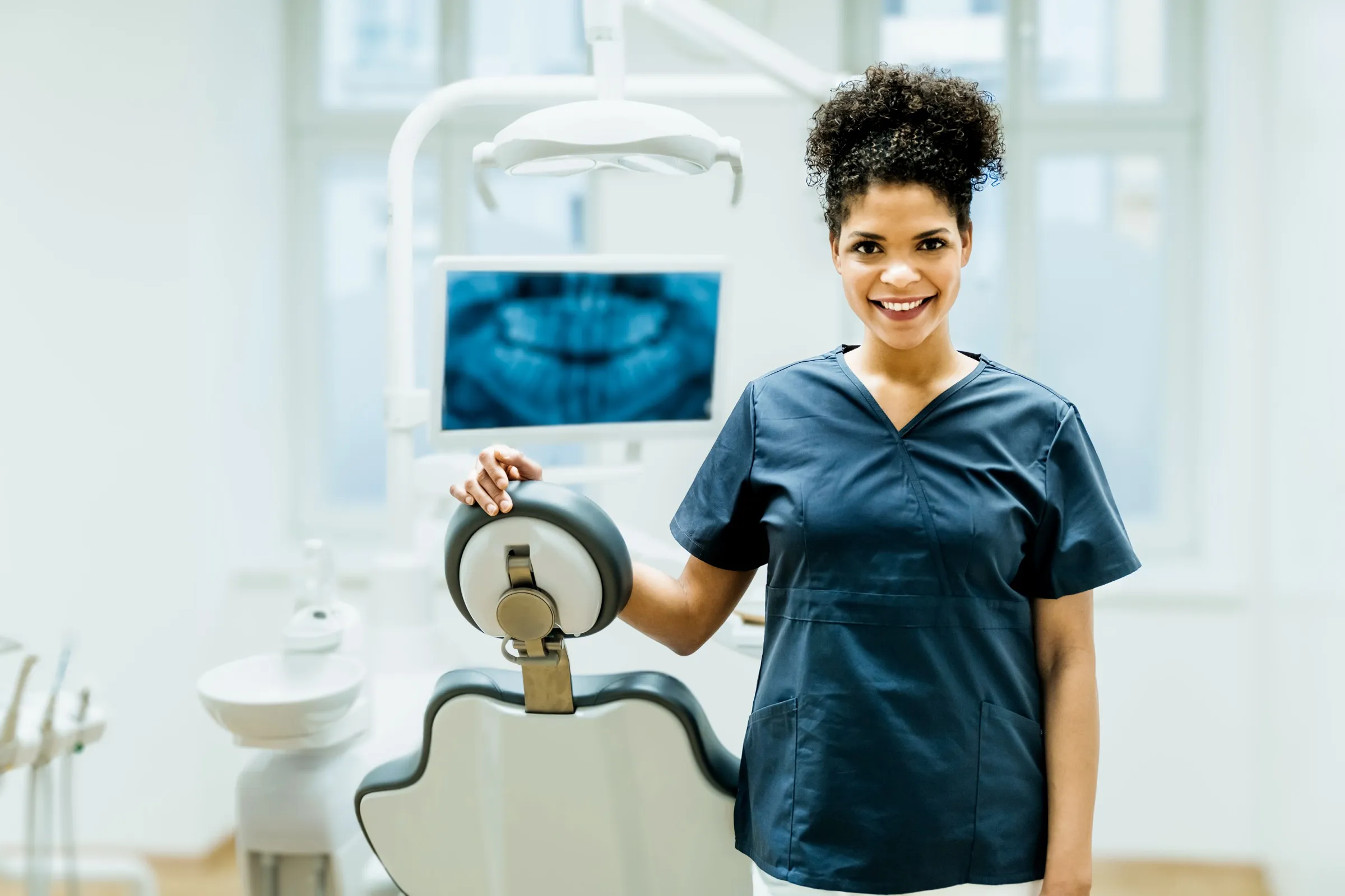Dentist standing beside a dental chair and X-ray display