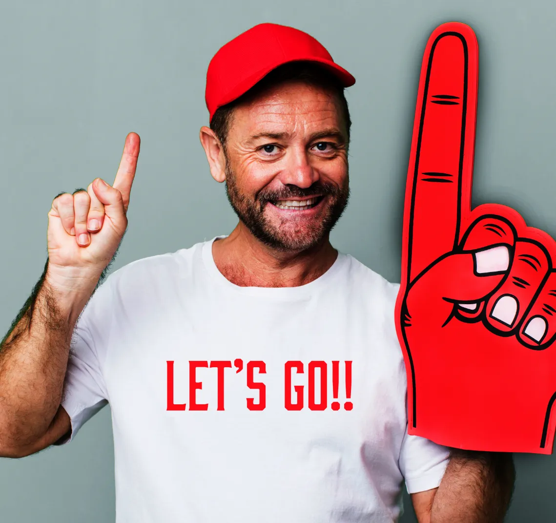 Smiling man in a red cap holding up a large red foam finger.