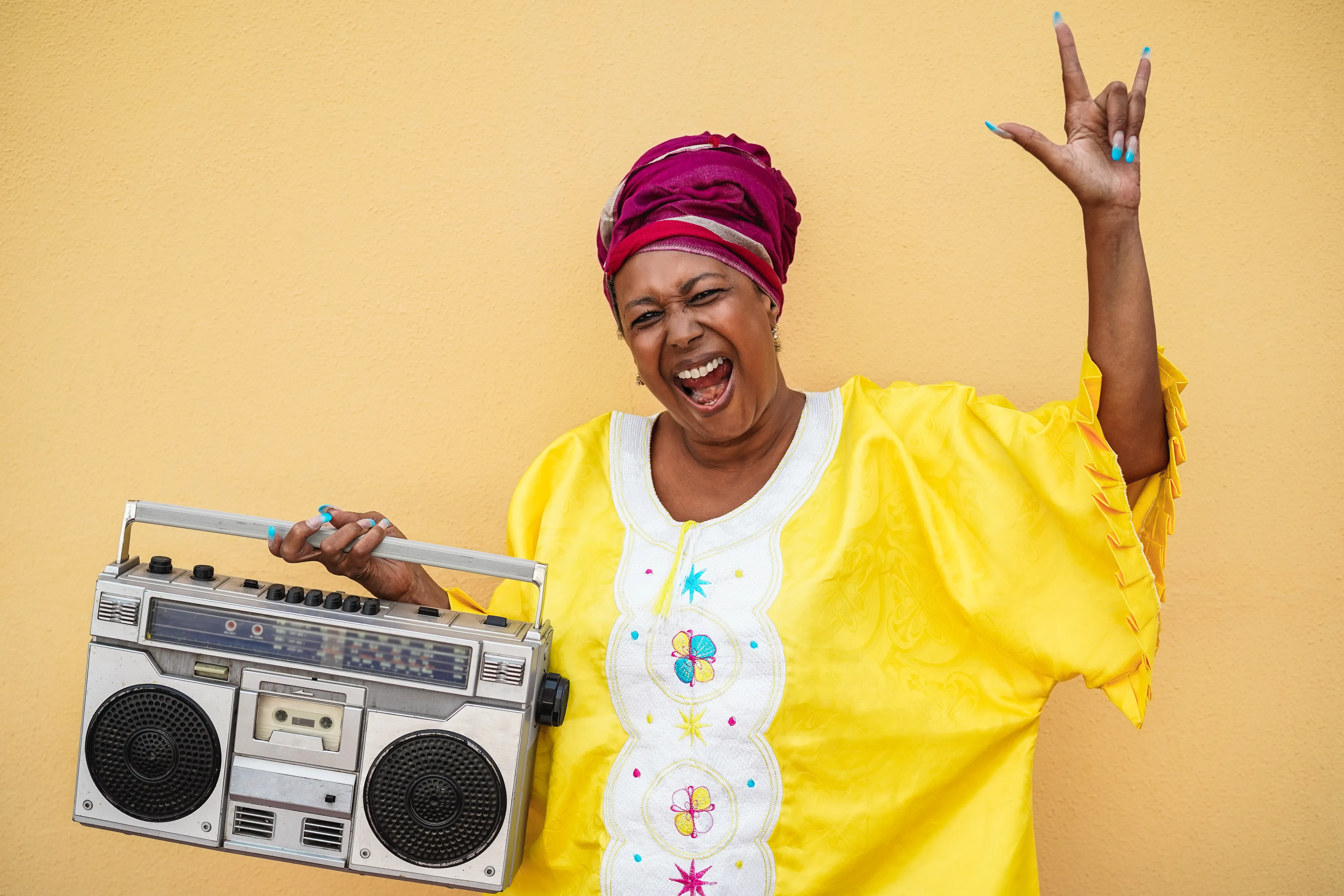 Joyful woman in a bright yellow outfit holding a vintage boombox and raising her hand.