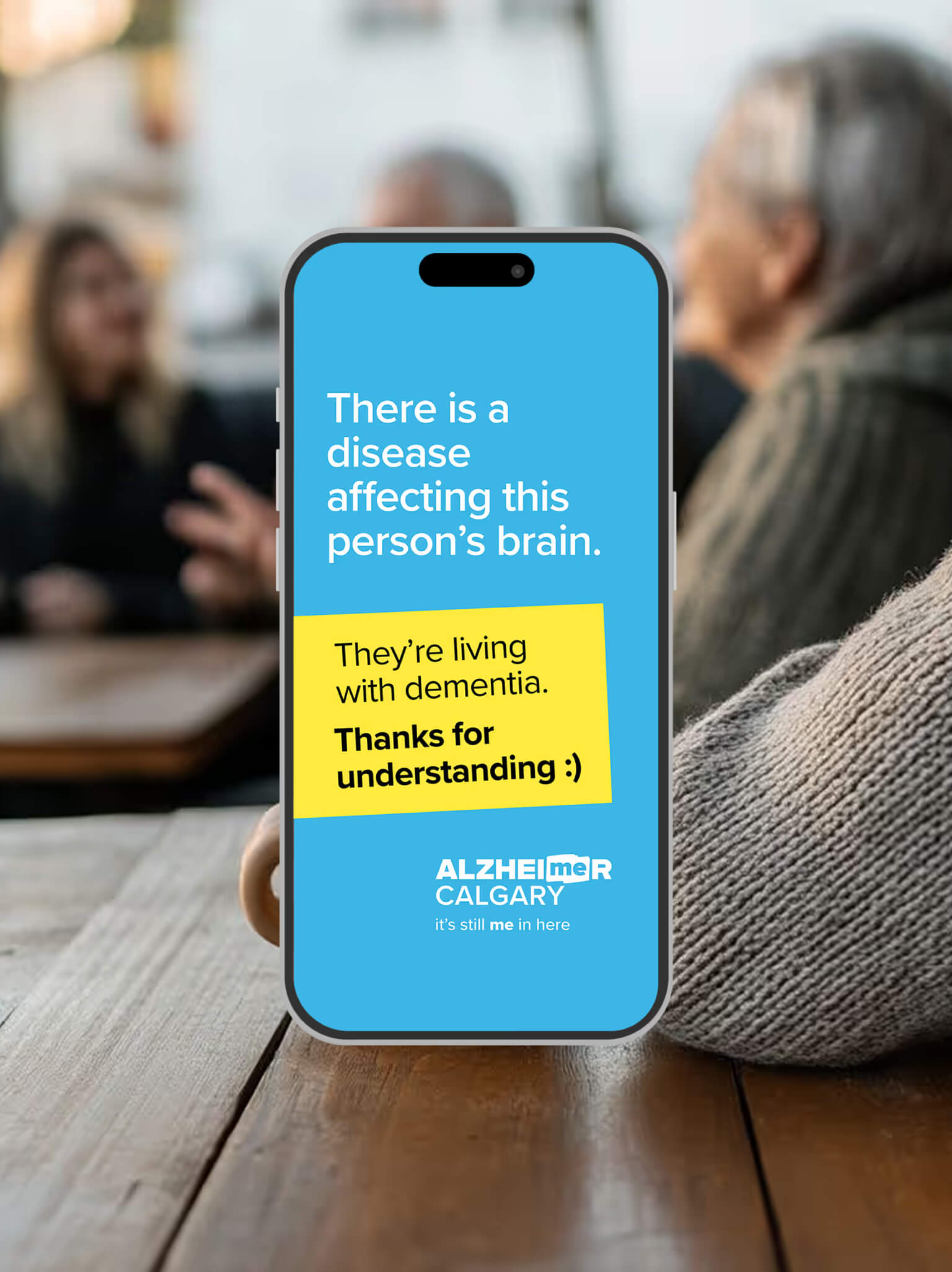 Smartphone displaying an Alzheimer Calgary dementia awareness card that reads, “They’re living with dementia. Thanks for understanding.”