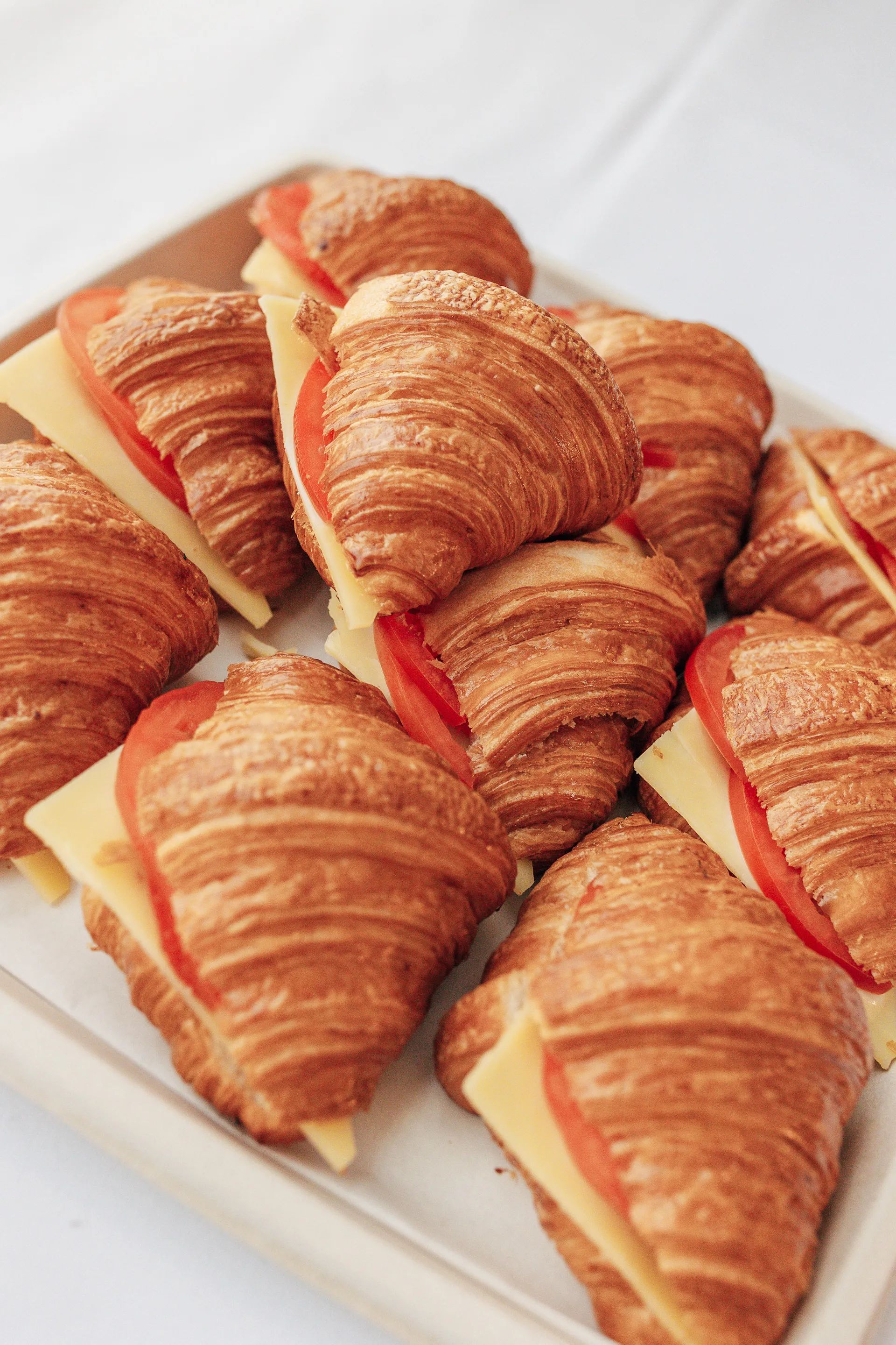 Tray of croissant sandwiches filled with slices of cheese and tomato.
