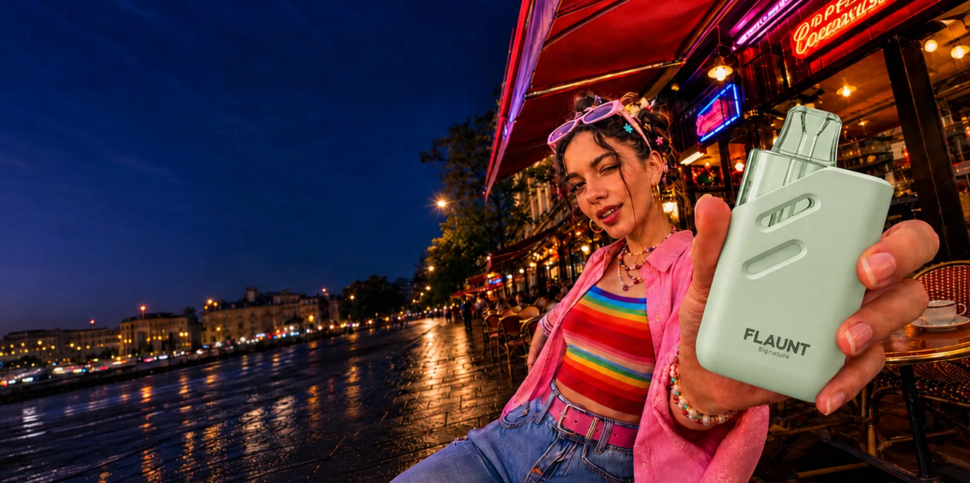 A person holding a Flaunt Signature device on a waterfront promenade at night