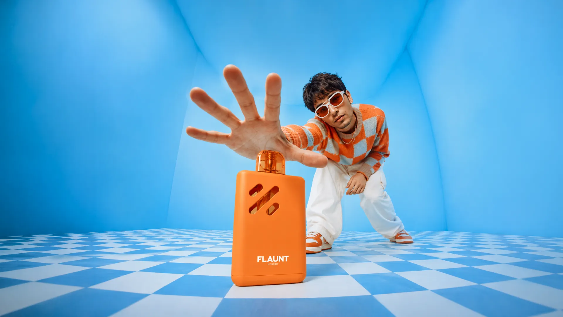 A person in an orange checked jumper reaching past a large orange Flaunt device in a blue checkerboard room