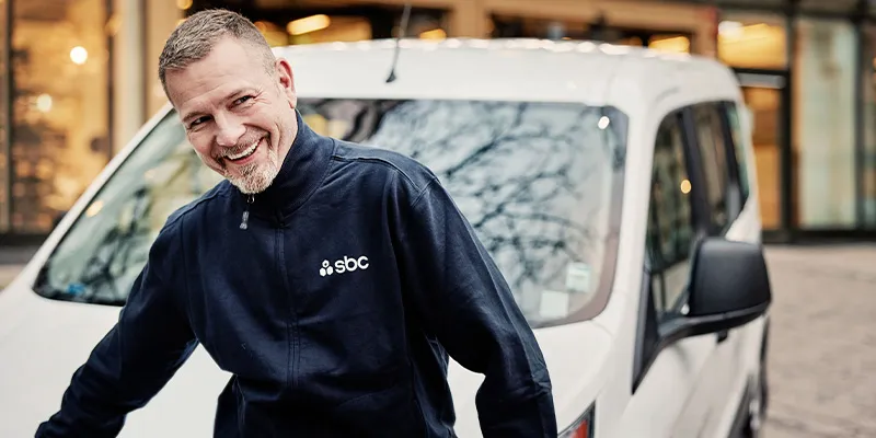 Leende SBC-medarbetare i mörkblå jacka framför en vit servicebil