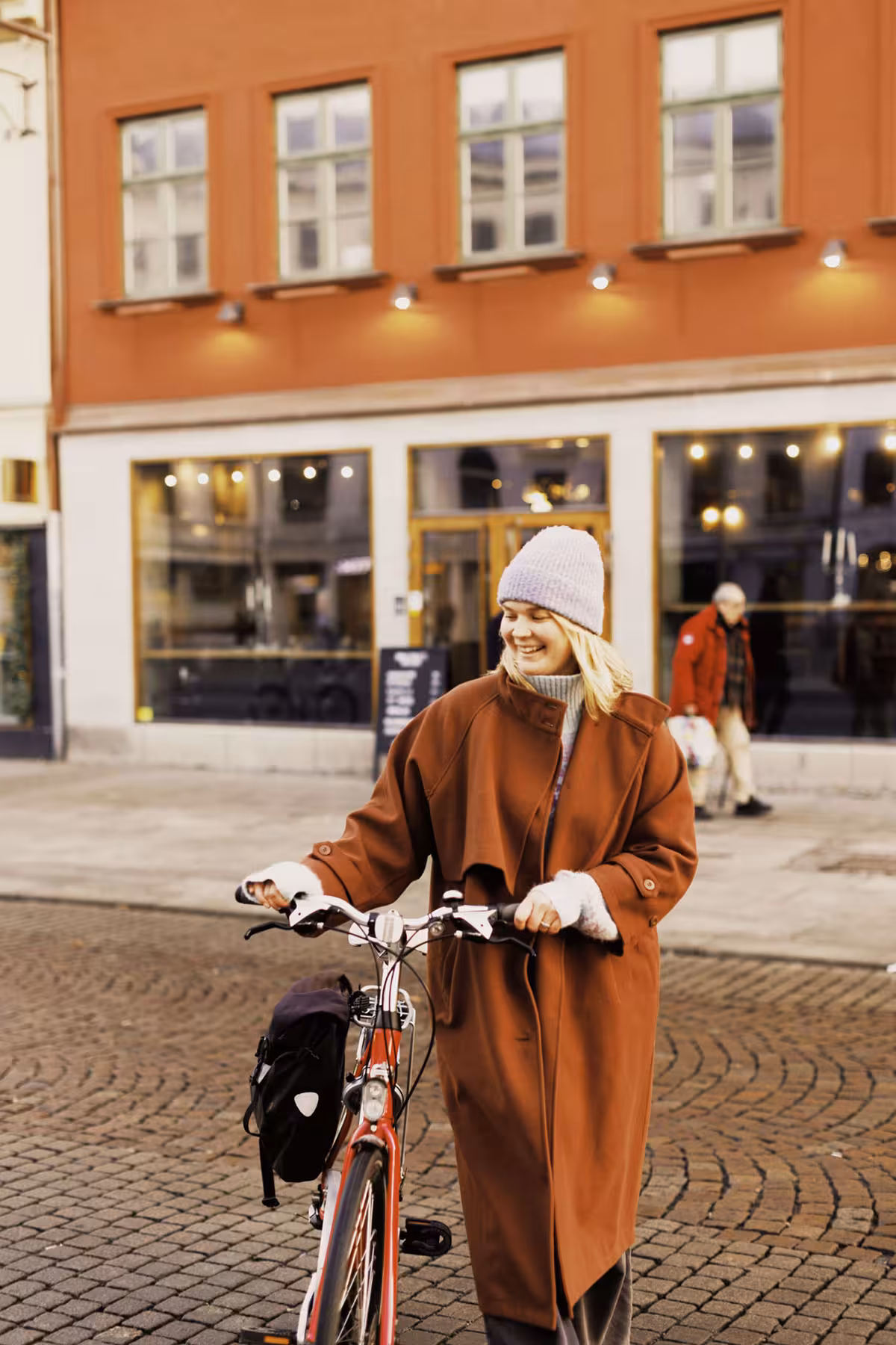 Person promenerar med cykel utanför flerbostadshus i stadsmiljö.