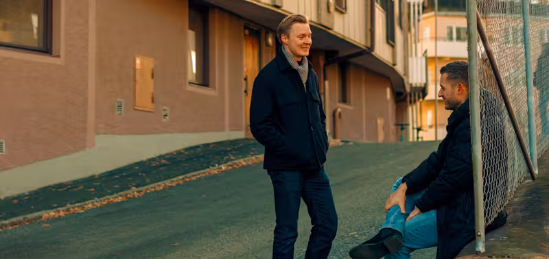     Två personer har ett samtal utanför ett bostadshus.