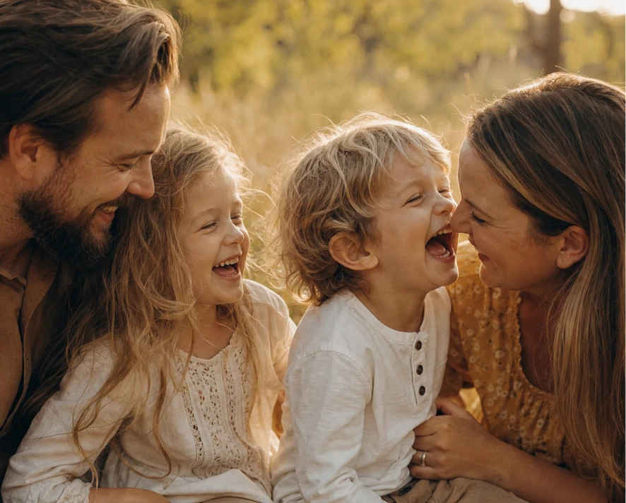 Família de quatro ao ar livre, pais e dois filhos pequenos a sorrir num momento de alegria.